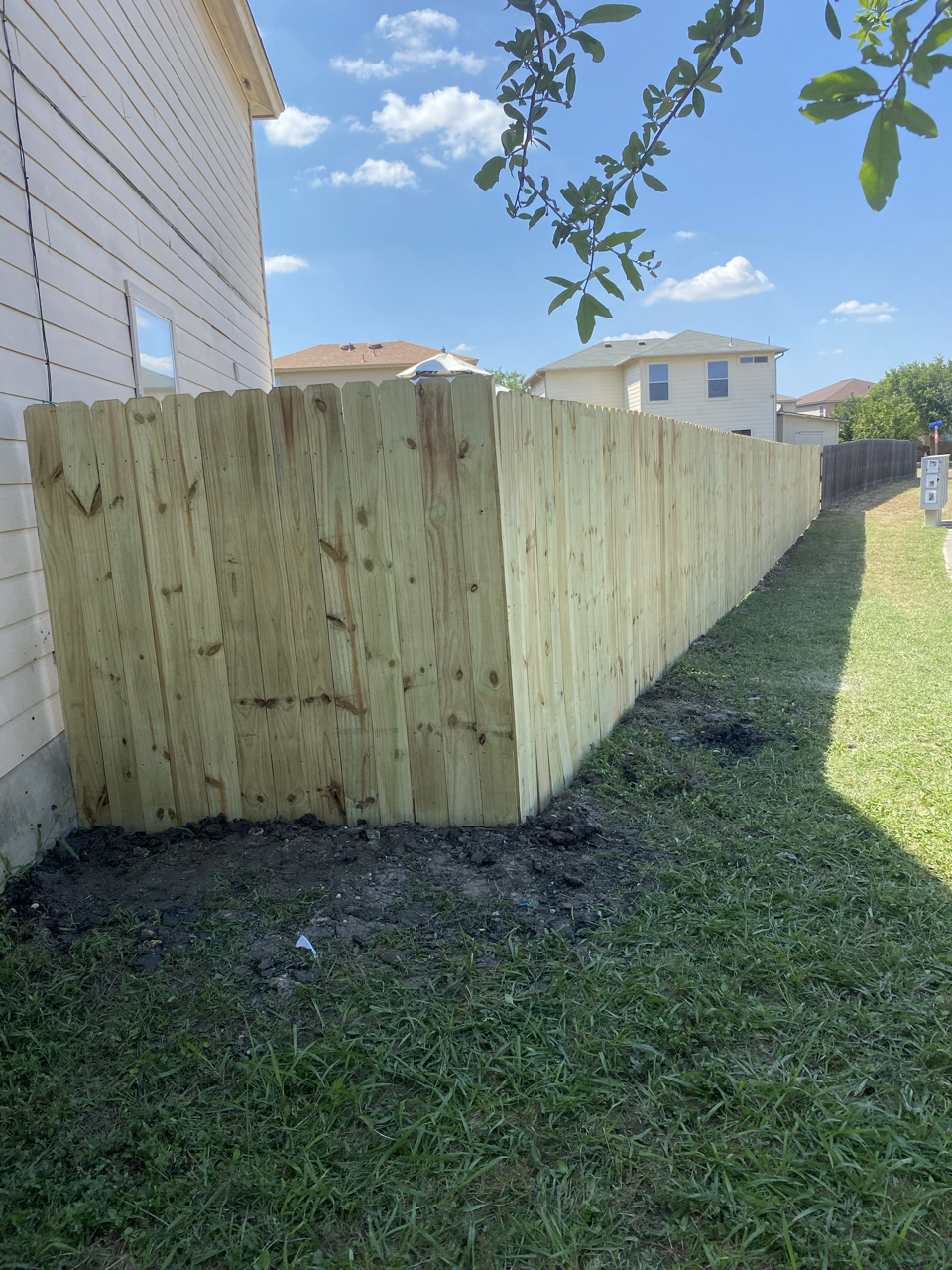 Wooden fence along the side of a house on a sunny day with a blue sky and some clouds.