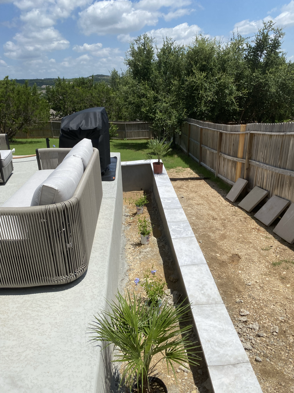 Partially completed backyard renovation with a patio, potted plants, and a wood privacy fence under a partly cloudy sky.