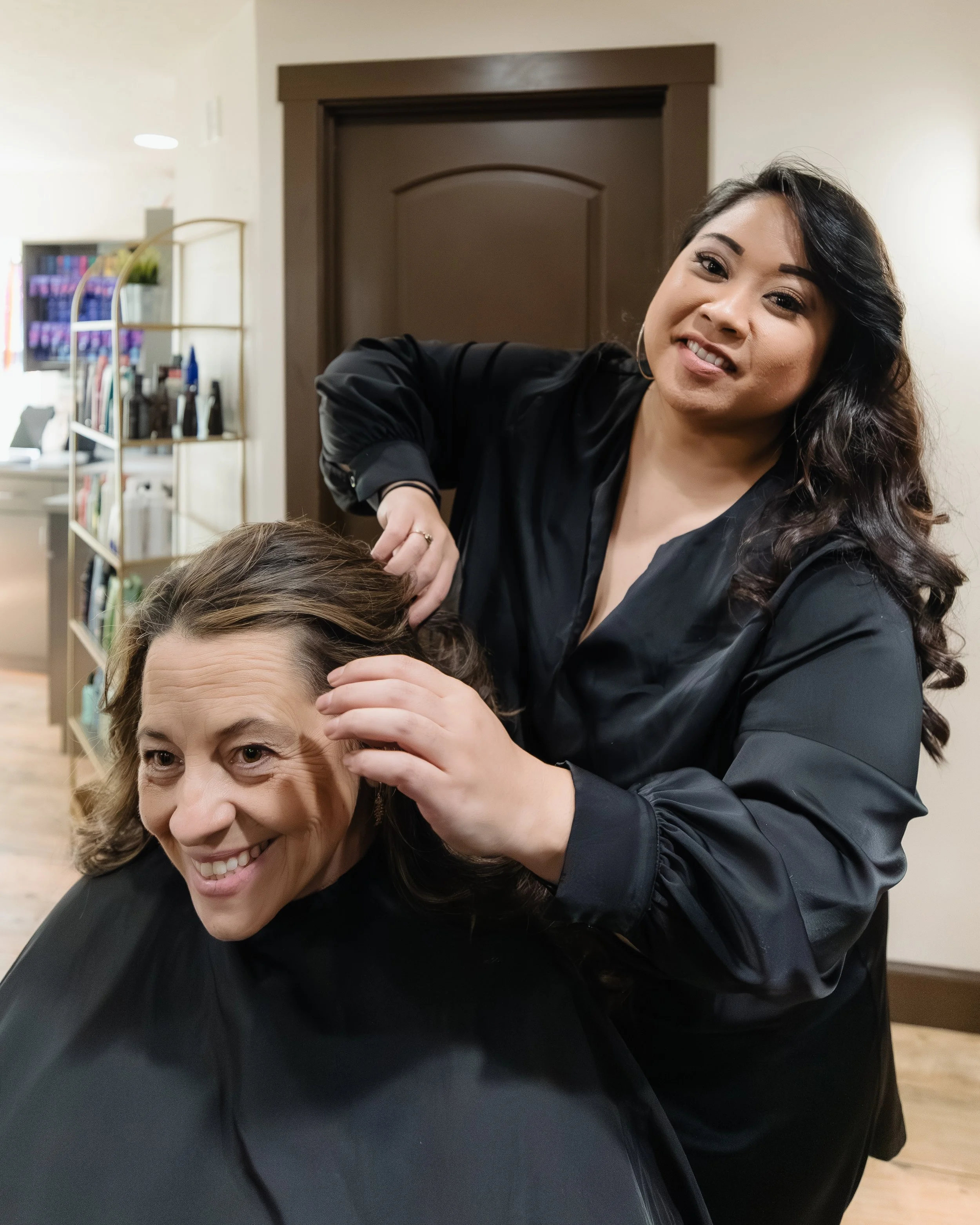 A woman with dark hair getting her hair styled by a hairstylist in a salon.