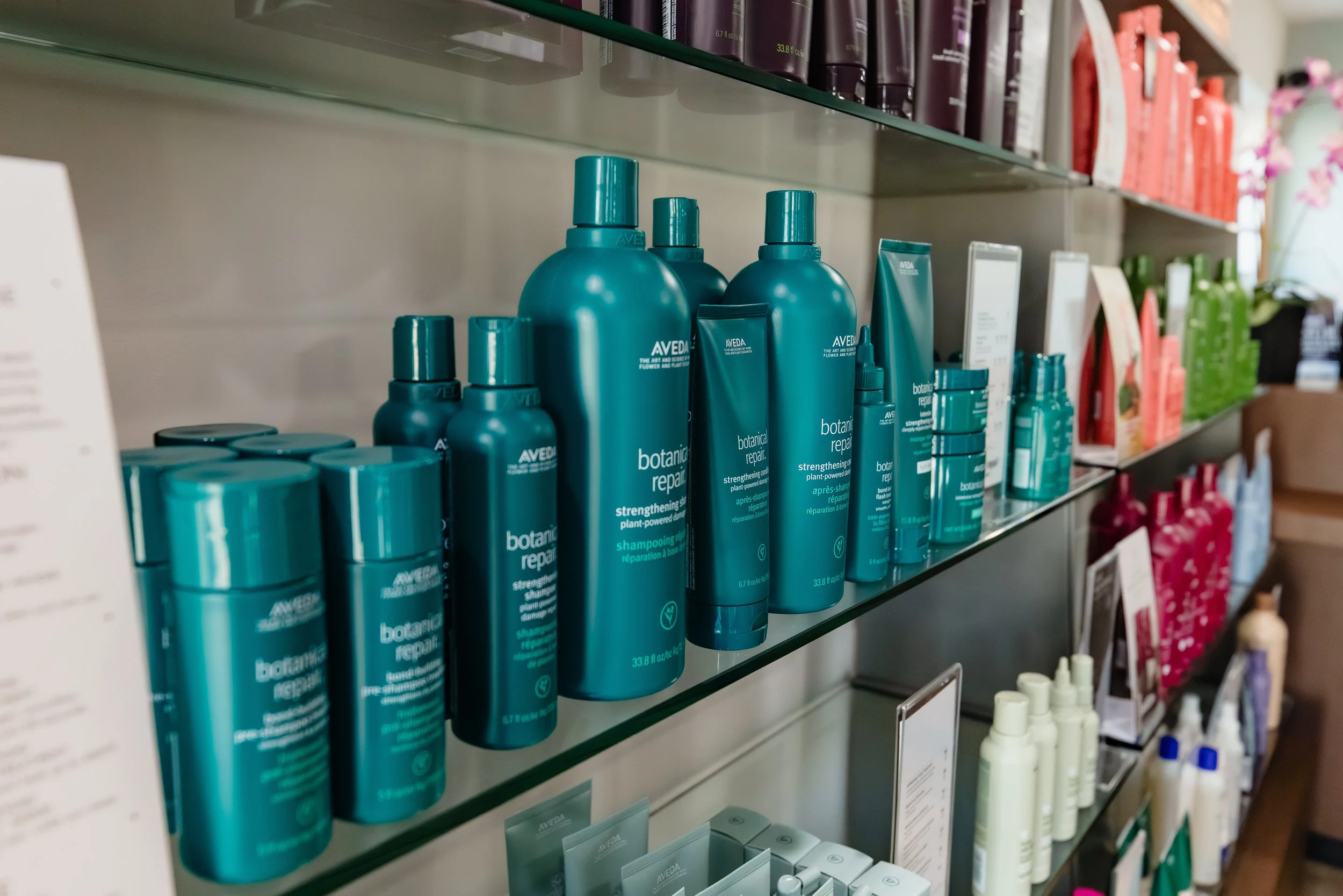 Shelf displaying various hair care products including large teal bottles of Aveda Botanical Repair strengthening shampoo.