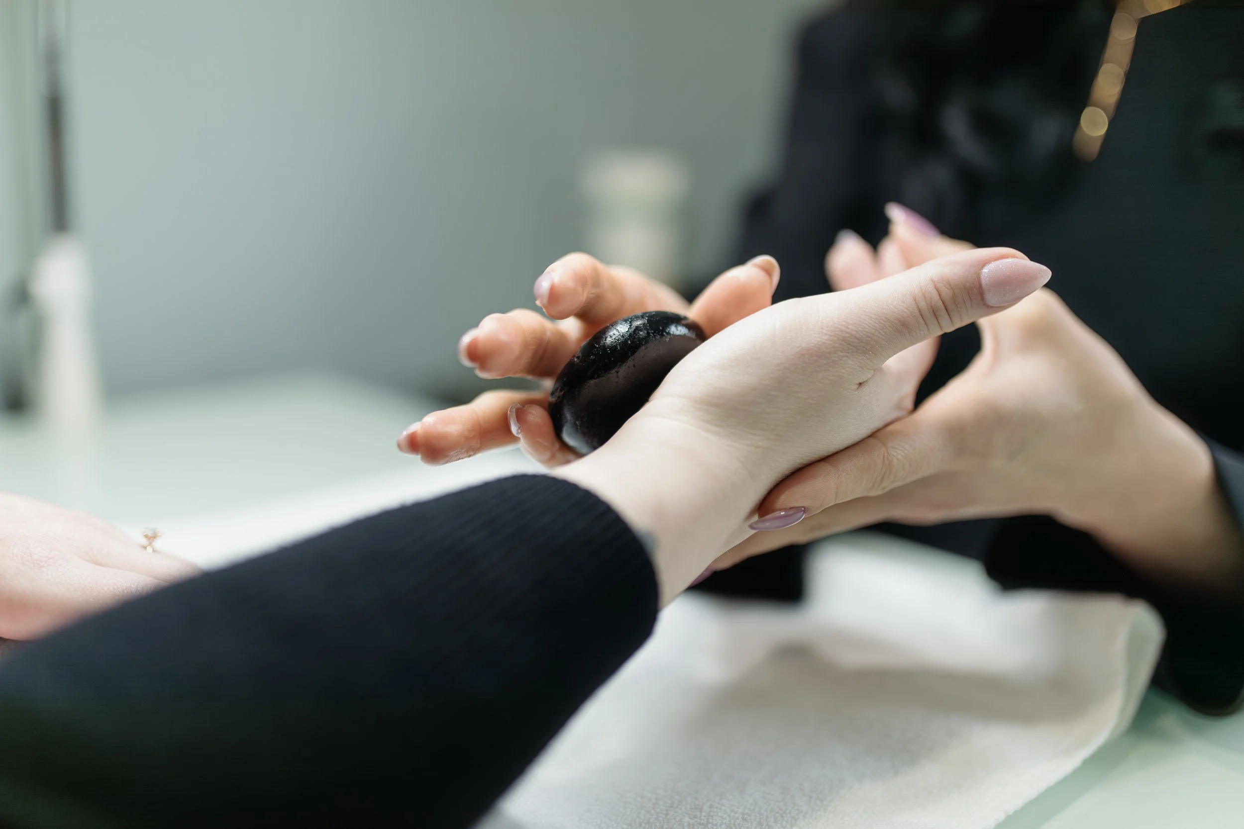 Close-up of a person's hands during a manicure, with one hand holding a black stone and nails painted with a French manicure.
