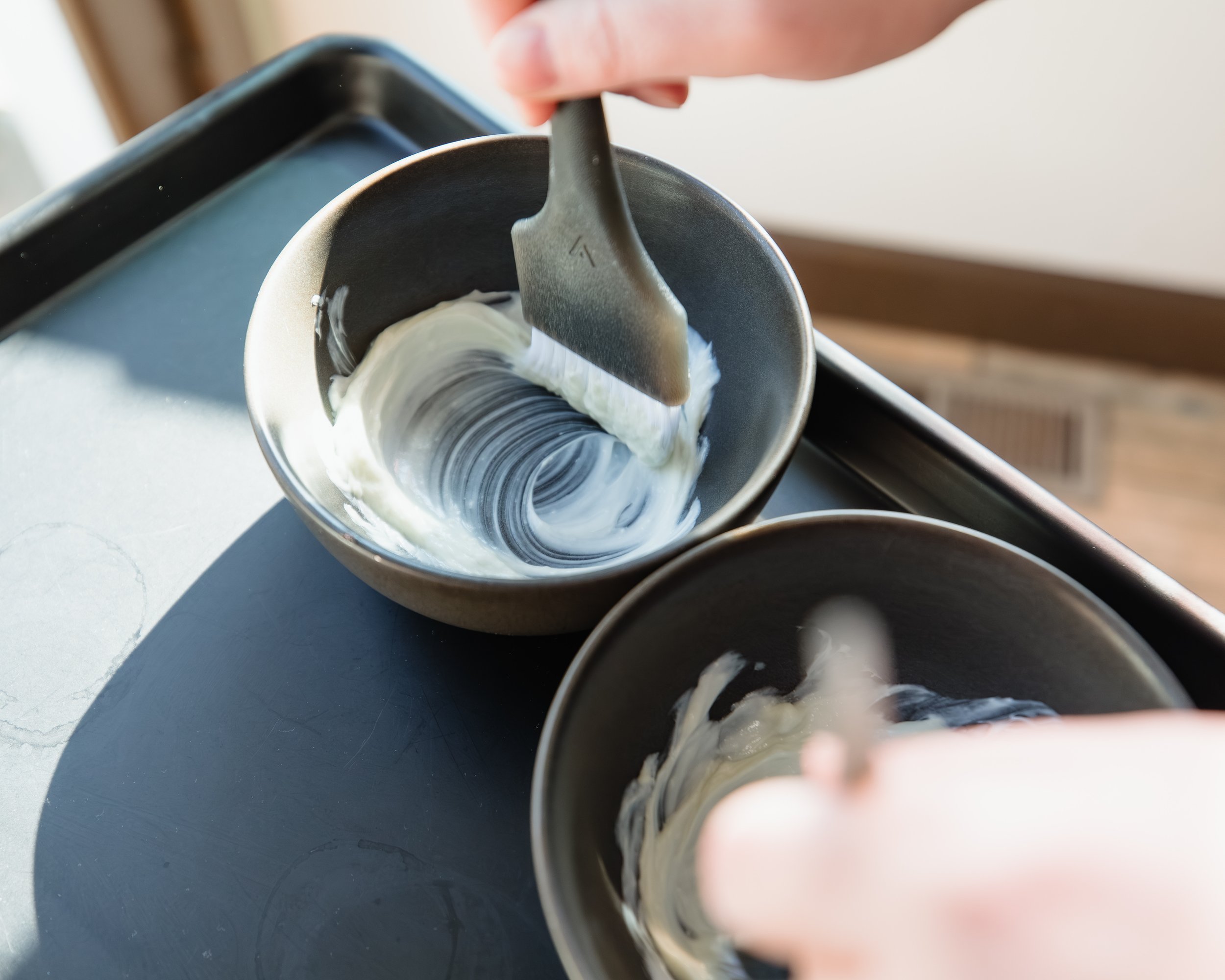 Person scraping the inside of ceramic bowls with a metal spatula while placing the scraped material into smaller bowls.