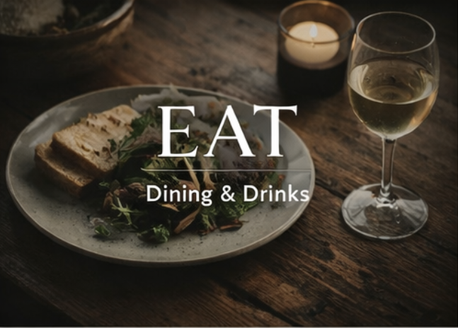 A dinner setting with a plate of sandwiches and salad, a glass of white wine, and a lit candle on a wooden table.