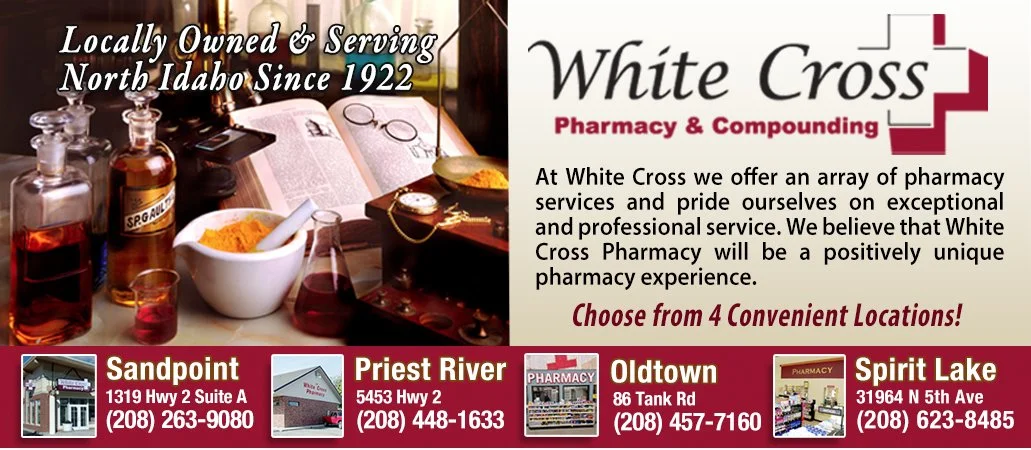 An advertisement for White Cross Pharmacy & Compounding highlighting its locally owned status since 1922 and four convenient locations: Sandpoint, Priest River, Oldtown, and Spirit Lake, Idaho. The ad features images of pharmacy supplies, a mortar and pestle, and pharmacy storefronts with their addresses and phone numbers.