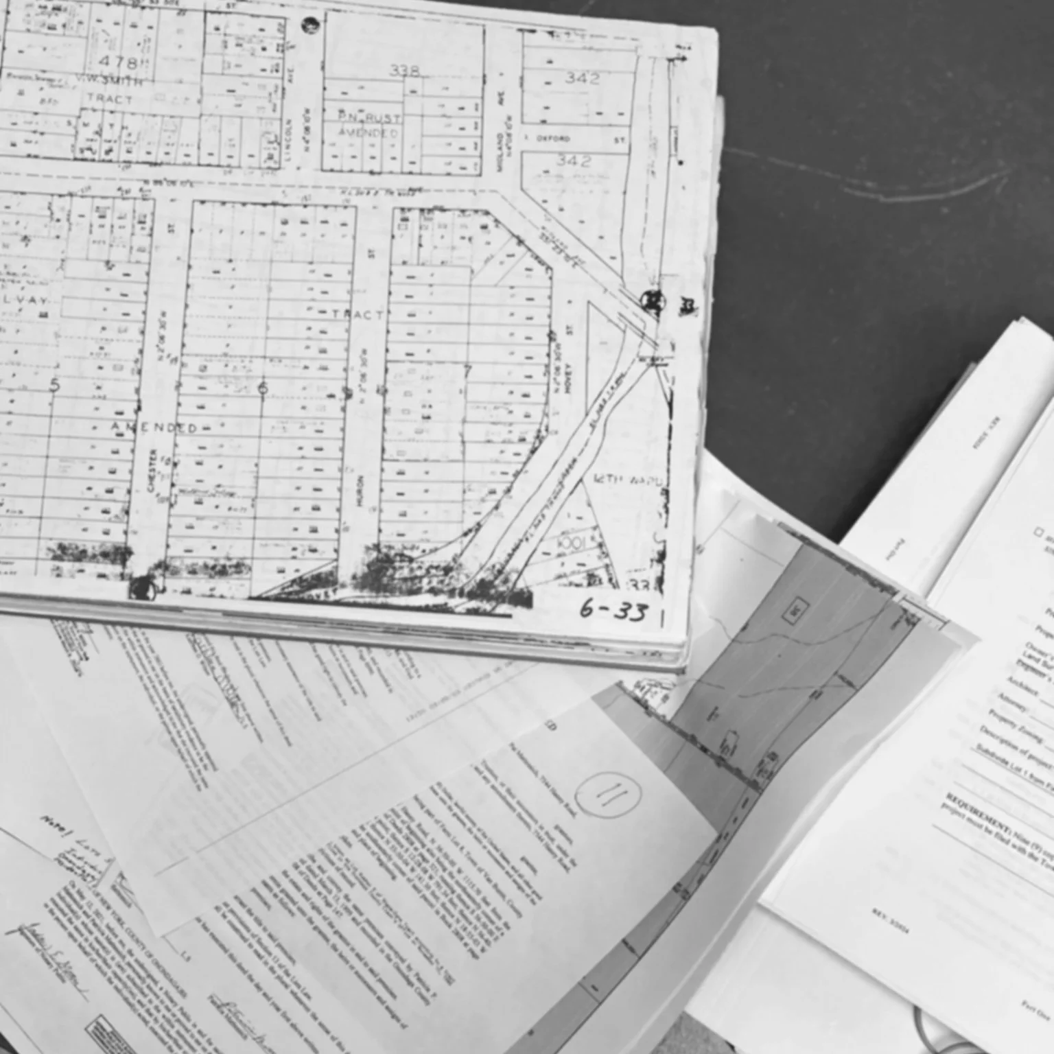 Black and white photograph of various detailed architectural and urban planning maps and blueprints spread out on a table.