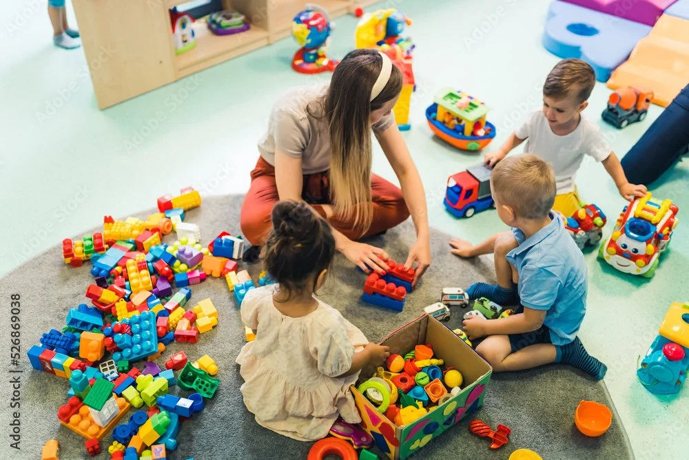 Childcare provider playing with children using colorful blocks and toy cars, keeping kids entertained while parents enjoy the event.