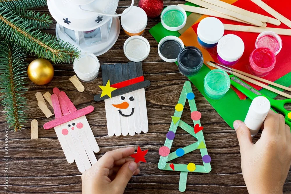 Christmas-themed childcare activity table with kids crafts, including painted popsicle stick snowmen, a small tree, and art supplies for fun holiday play during events.