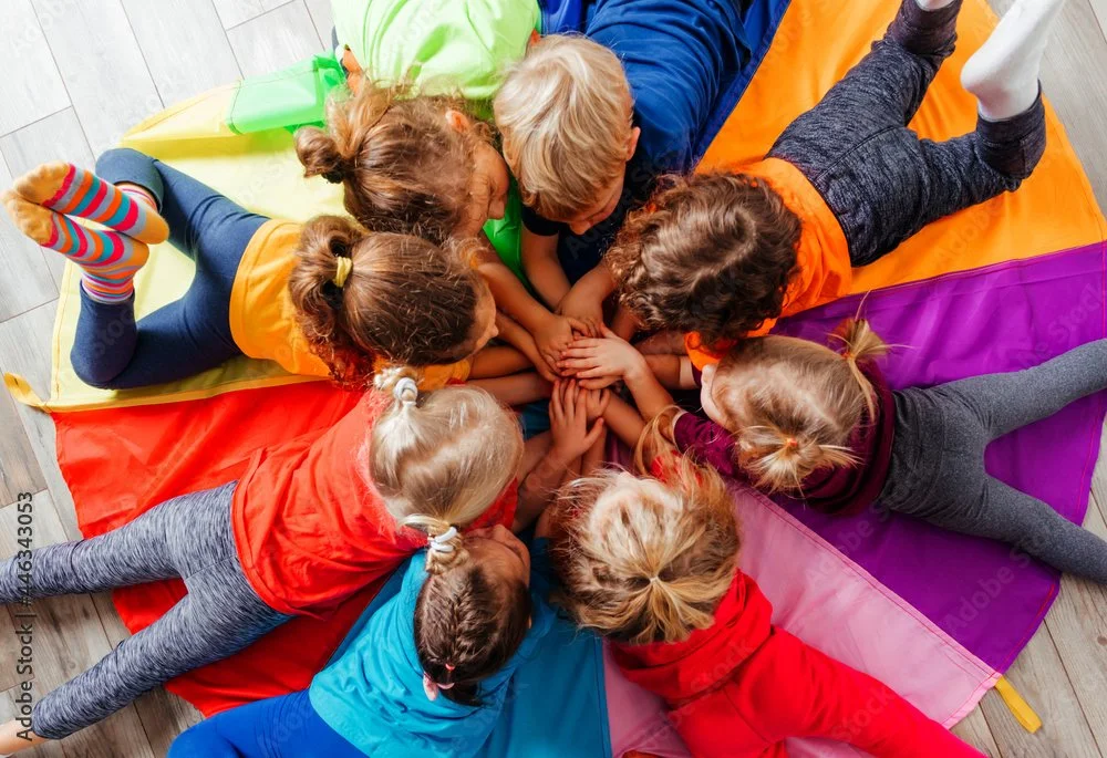 Group of children playing together with a colorful parachute, enjoying an interactive childcare activity during an event.