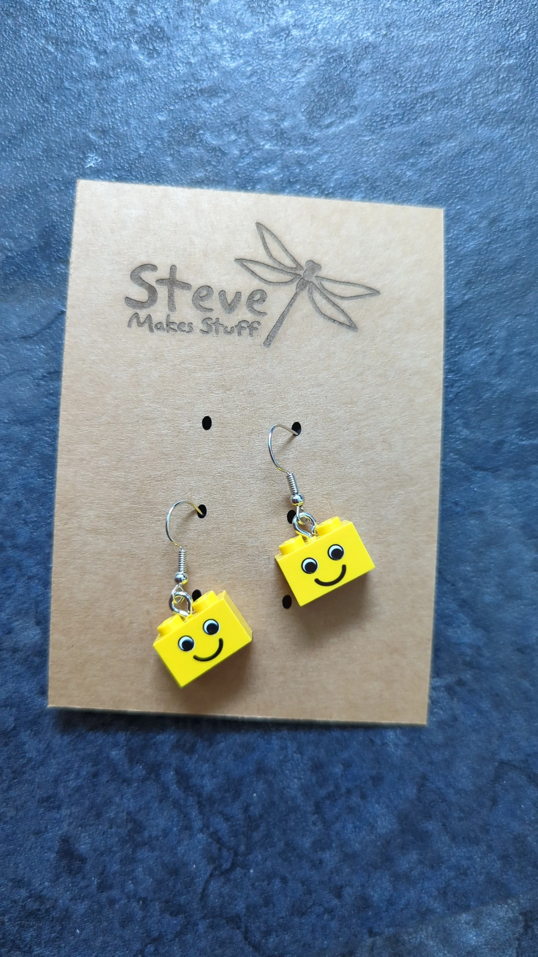 Yellow LEGO block earrings with smiling face design. 