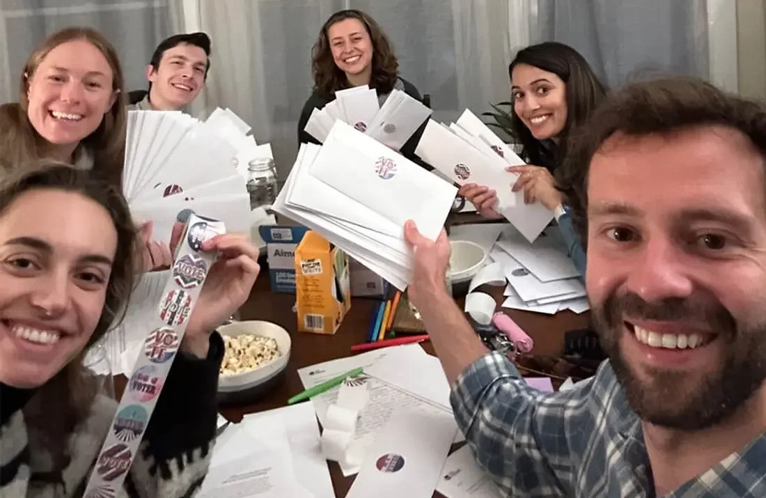A group of people sitting around a table with snacks, letters, and stamps.