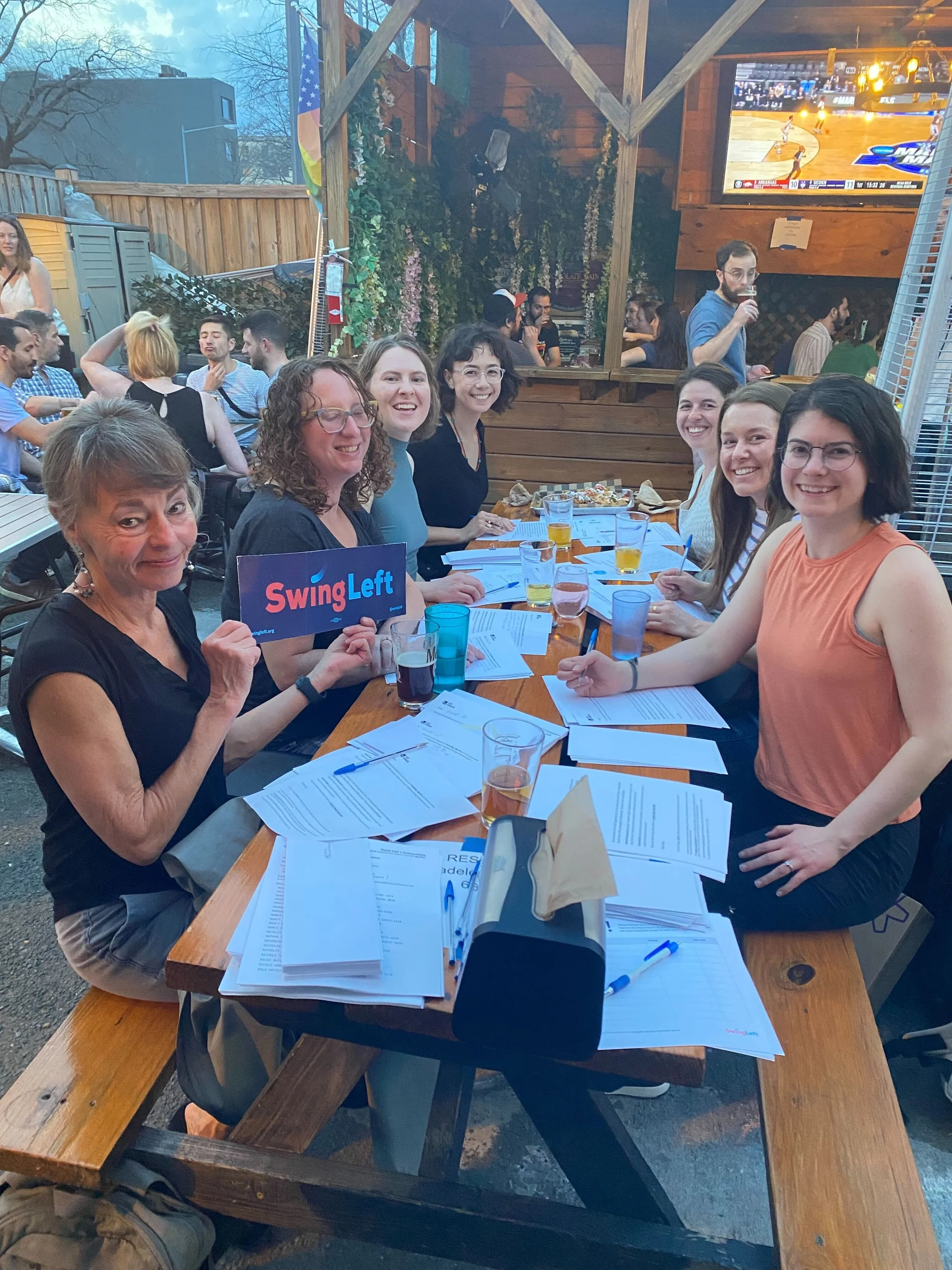 A group of Swing Left volunteers sit at a bar patio writing letters.