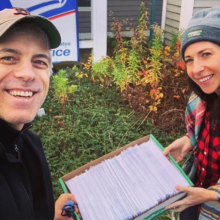 Two people standing in a yard holding a box of letters.