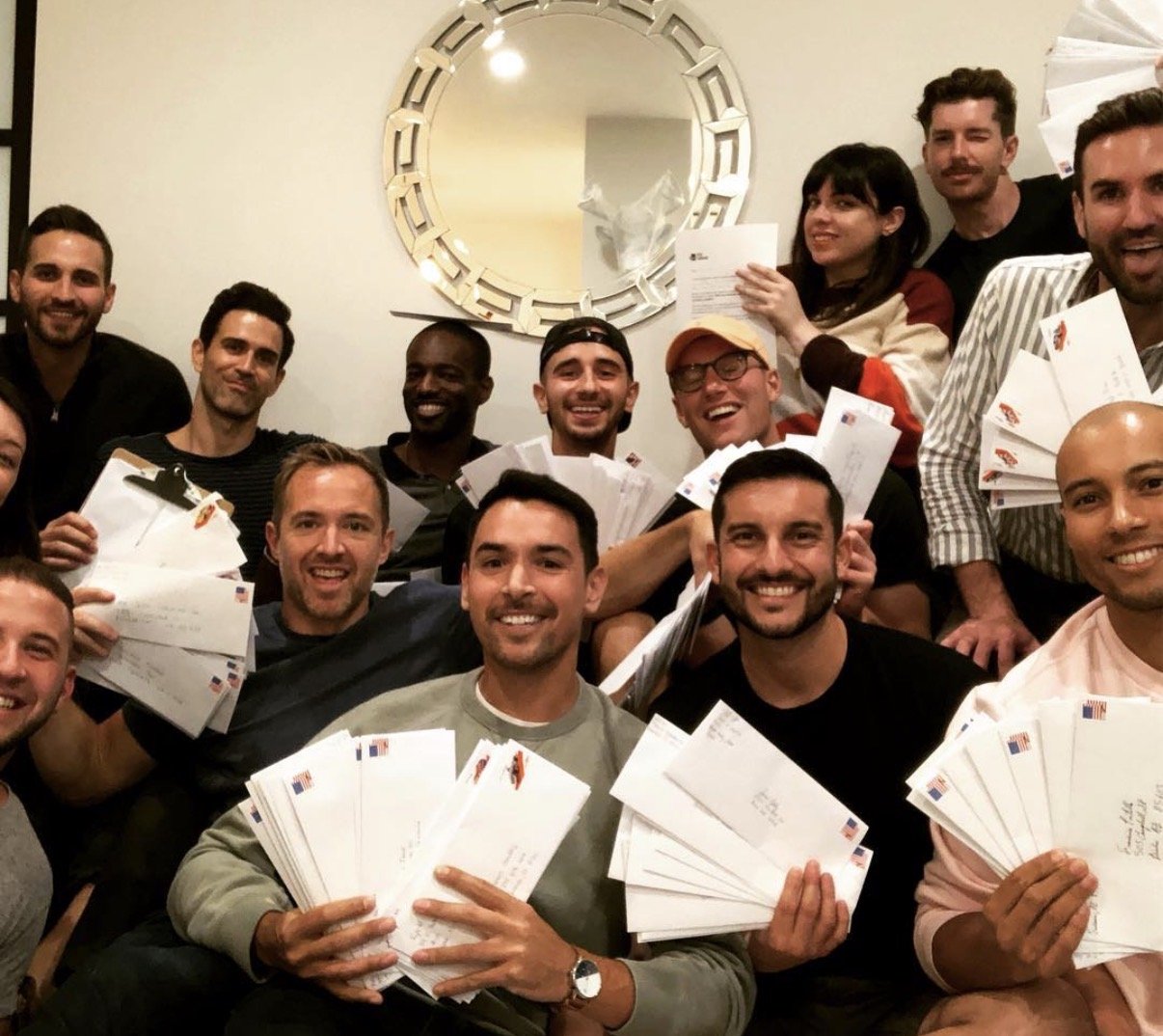 A group of smiling men holding up stacks of sealed and stamped letters.