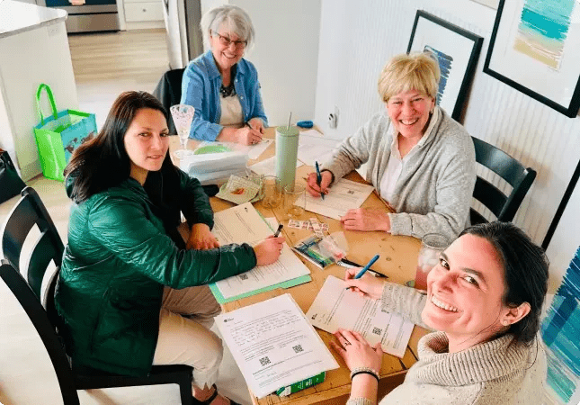 Four volunteers sitting at a dining room table writing letters and smiling.