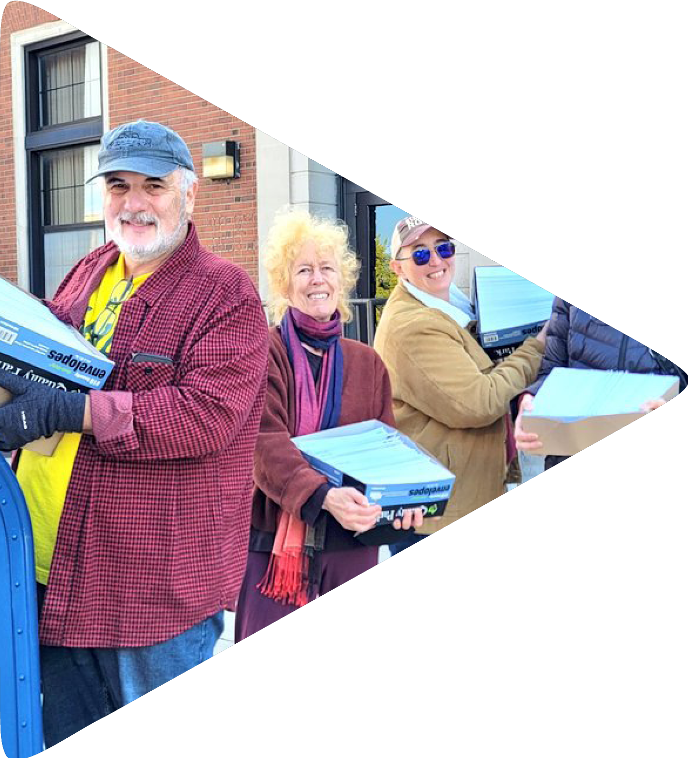 A group of people in coats and scarves holding large boxes of sealed letters in front of a post office.