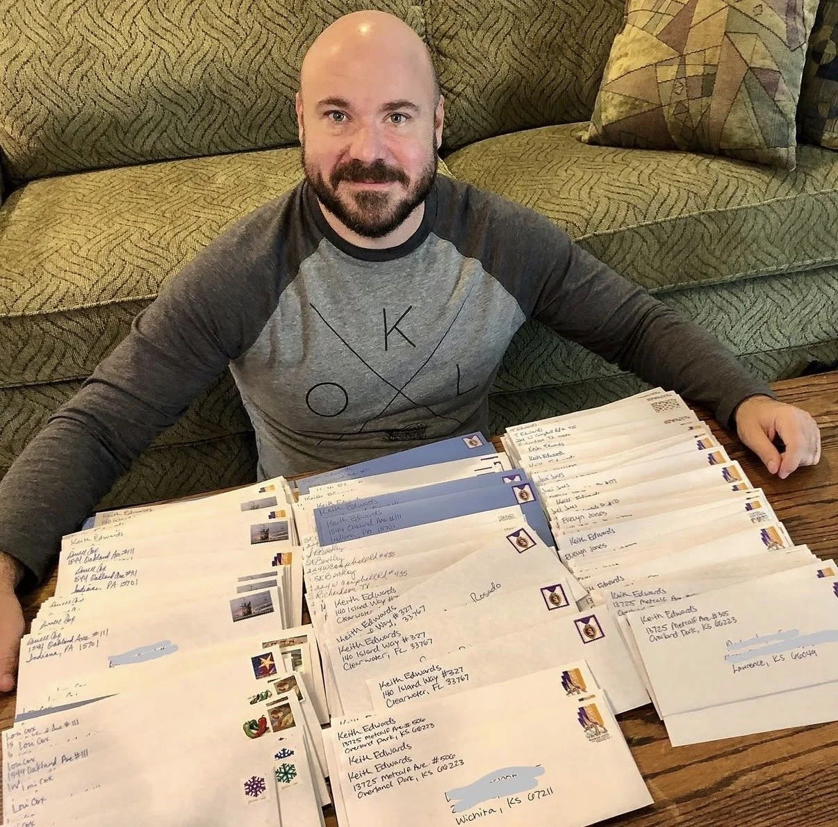 A man sits in front of a green couch on the floor with a large pile of stamped letters in front of him on a coffee table.
