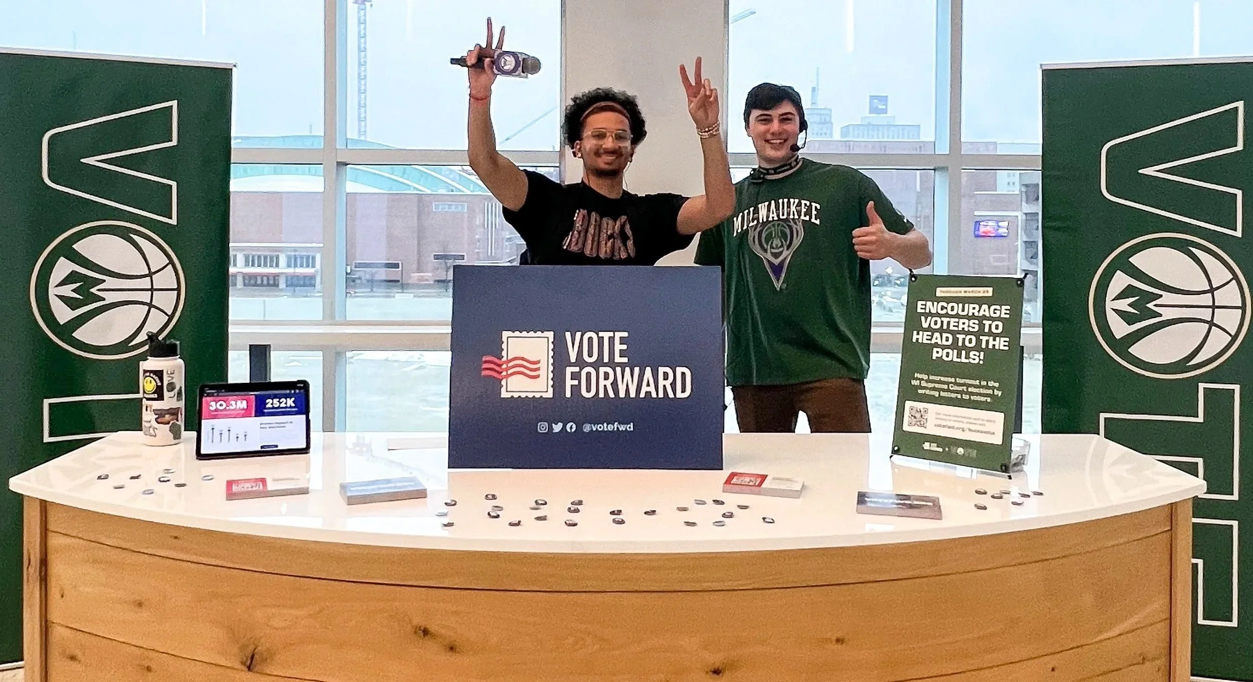 Two Milwaukee Bucks employees stand behind a table featuring Vote Forward signage.