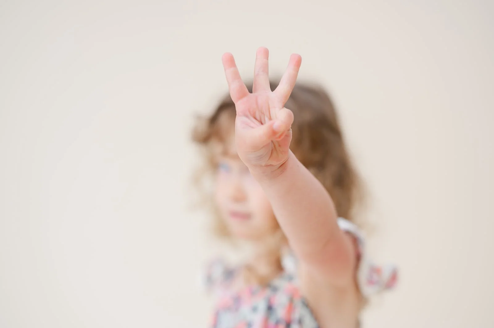 A young girl making a peace sign with her fingers, with her face slightly blurred in the background.