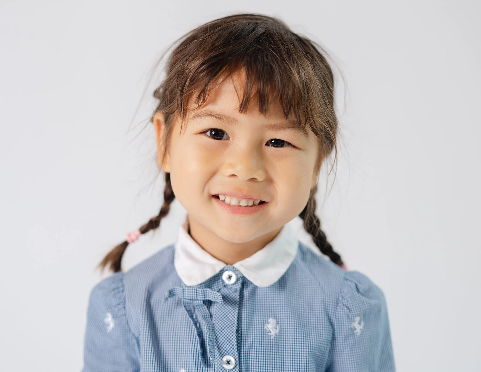 A young girl with braided hair, wearing a blue dress with a white collar, smiling against a plain white background.