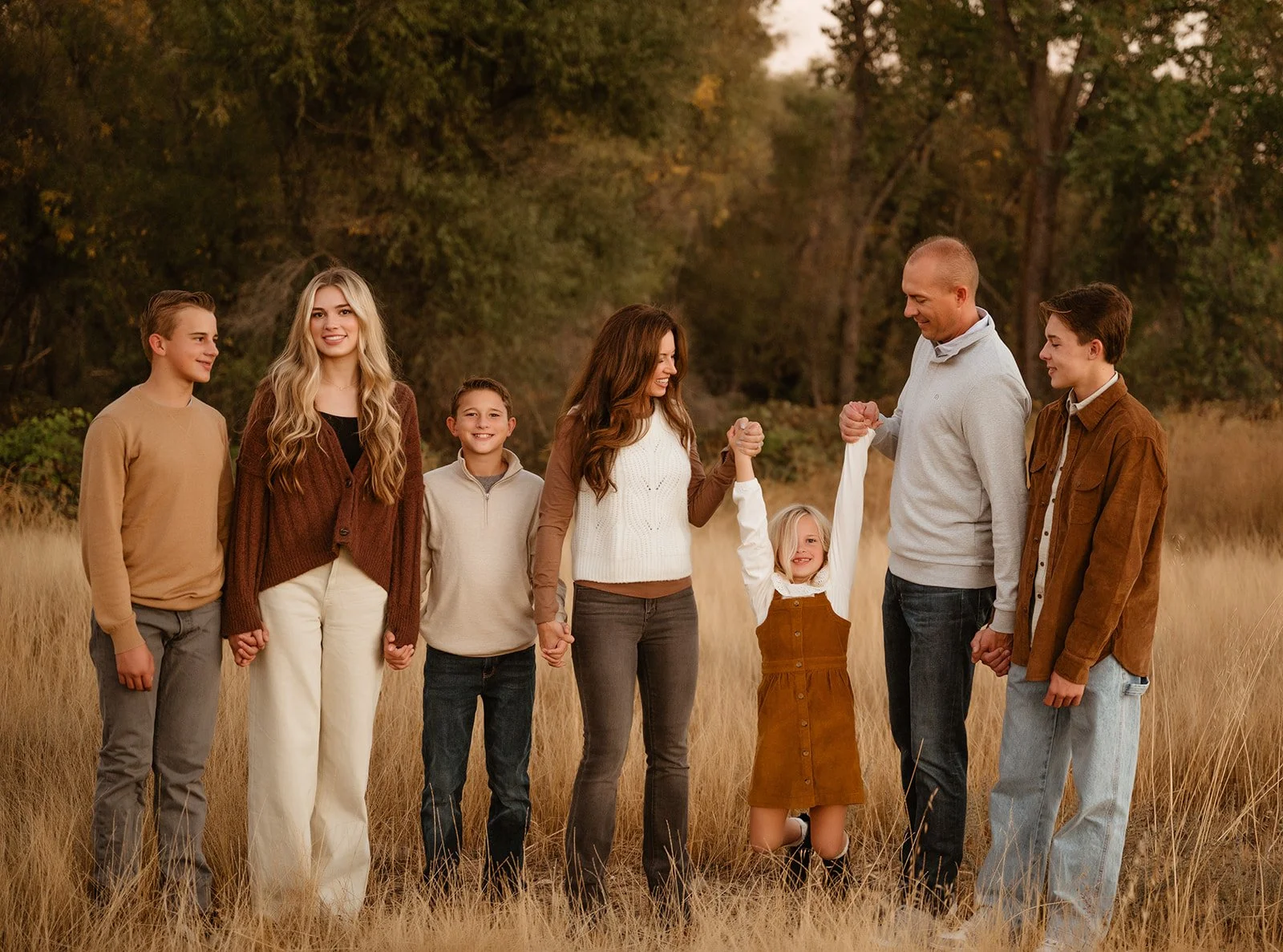 Family of seven holding hands in a field in autumn, smiling and celebrating outdoors.