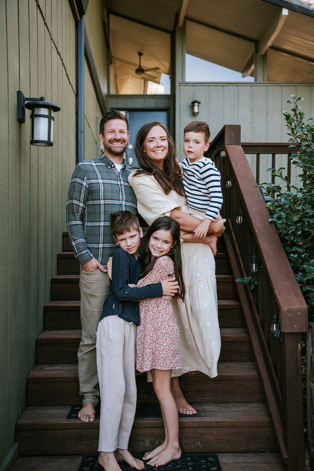 A family of five standing on a wooden staircase in front of their house, smiling and hugging each other.