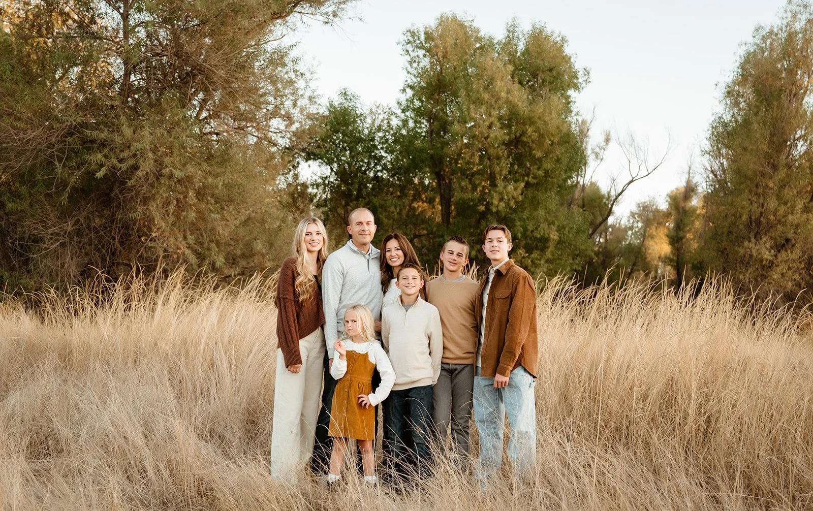 A family of seven standing in a field of tall, dry grass with trees in the background during daylight.