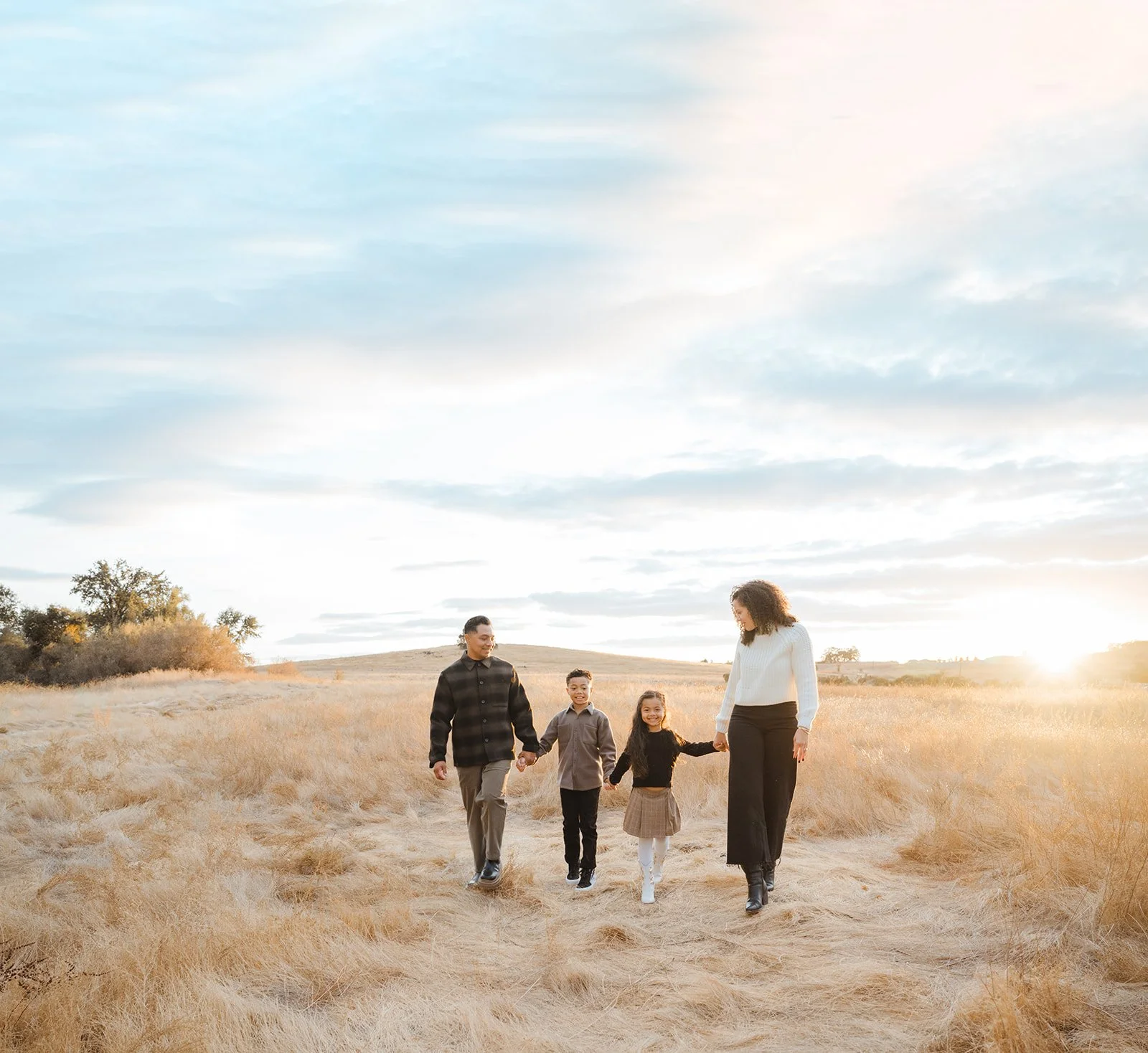 Family walking hand in hand through a grassy field during sunset.