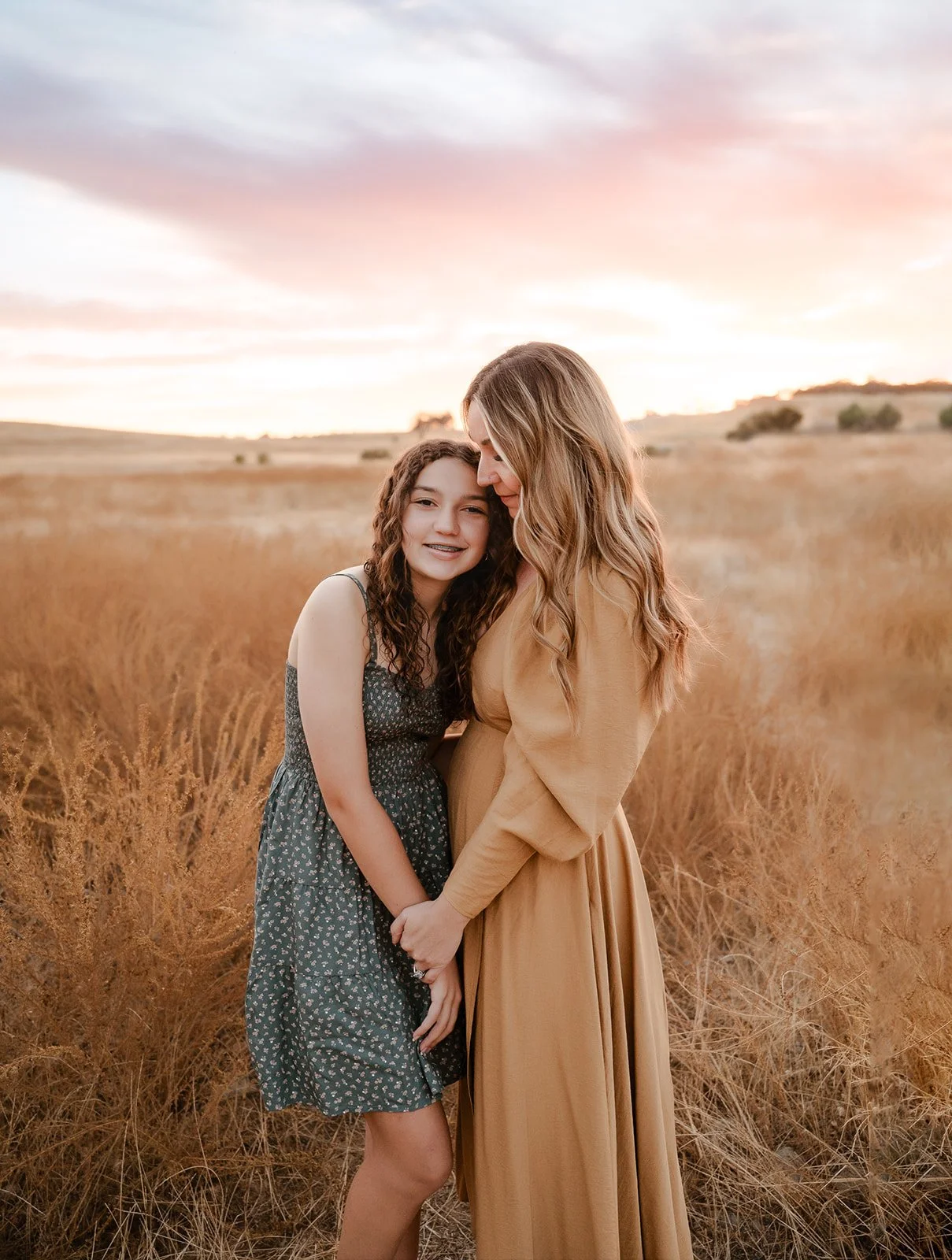 A woman and girl holding hands and hugging in a field at sunset.