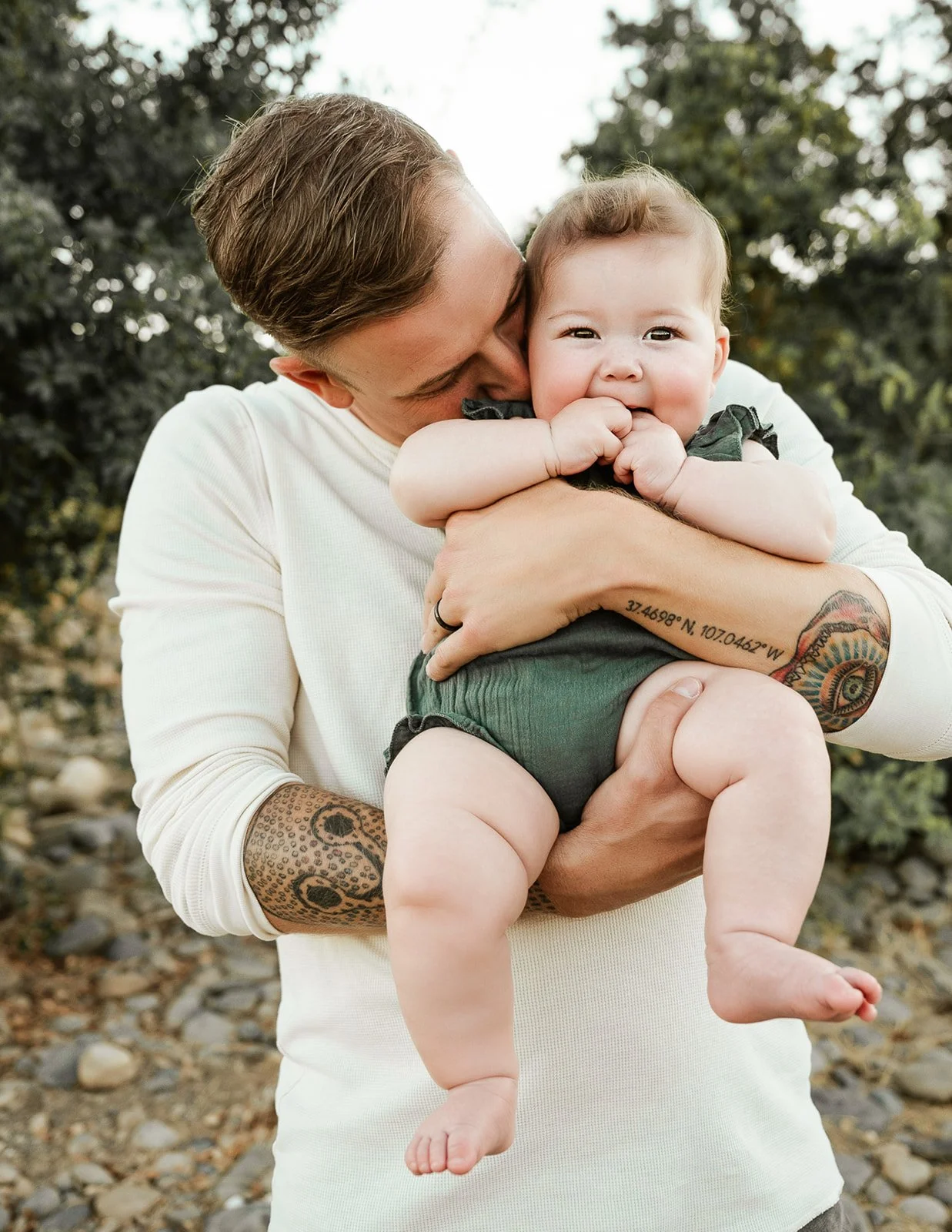 Father holding smiling baby during outdoor family session in Sacramento, California with natural light and relaxed setting
