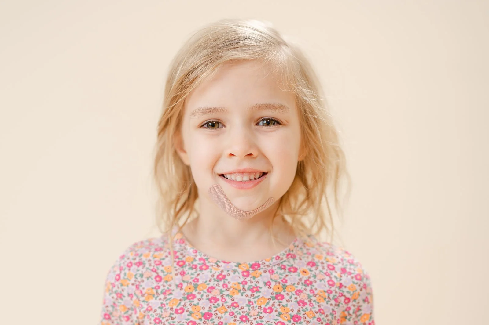 A young girl with blonde hair and blue eyes, smiling, wearing a floral shirt, against a plain light background.