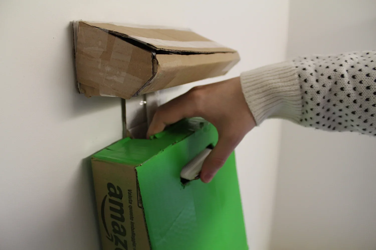 A person's hand holding a green marker, about to mark a green box on a white table. There are two cardboard boxes near the person's hand on the table.