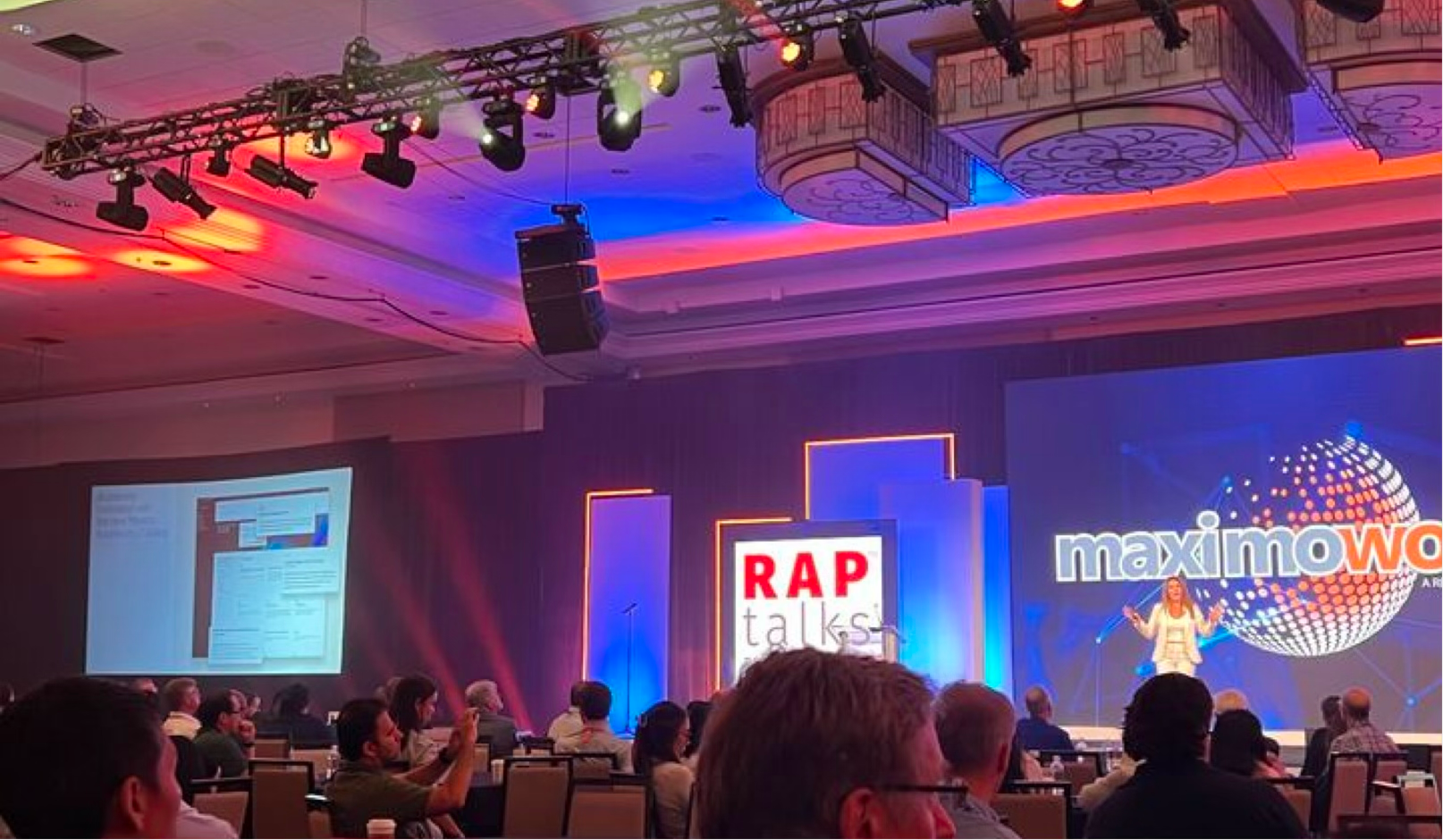 A conference with a stage, screen, and audience, featuring a presentation about rap and Maximo TV with a woman speaker on stage and colorful lighting.