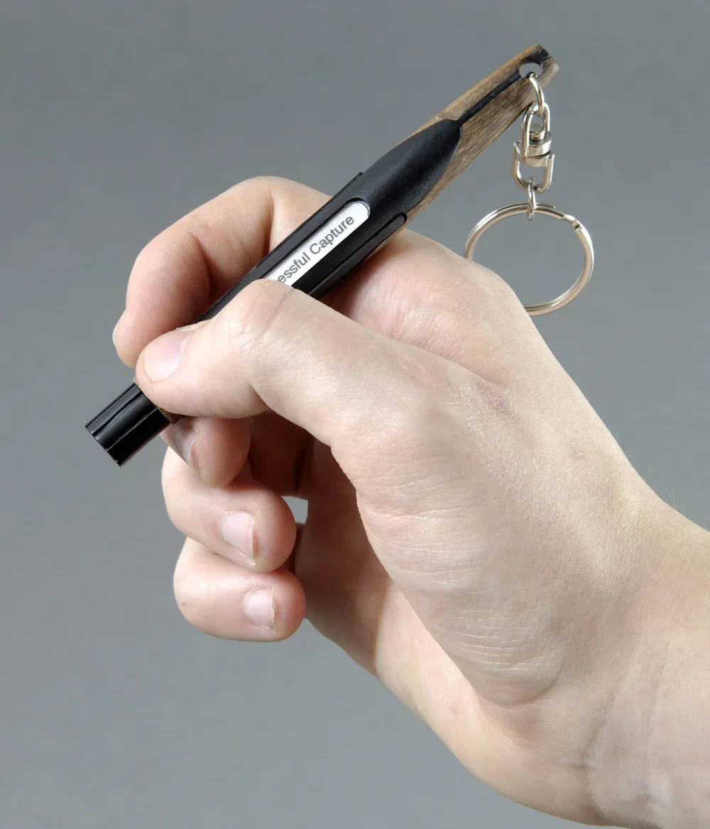 A hand holding a marker with a wooden clip-on attachment and a keychain hanging from it.