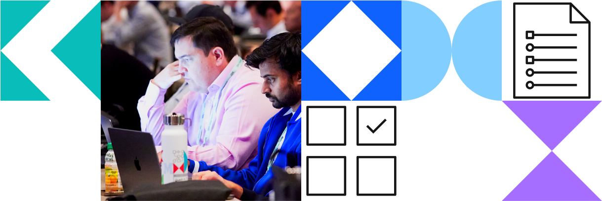 Two men working on laptops at a conference, surrounded by other attendees.