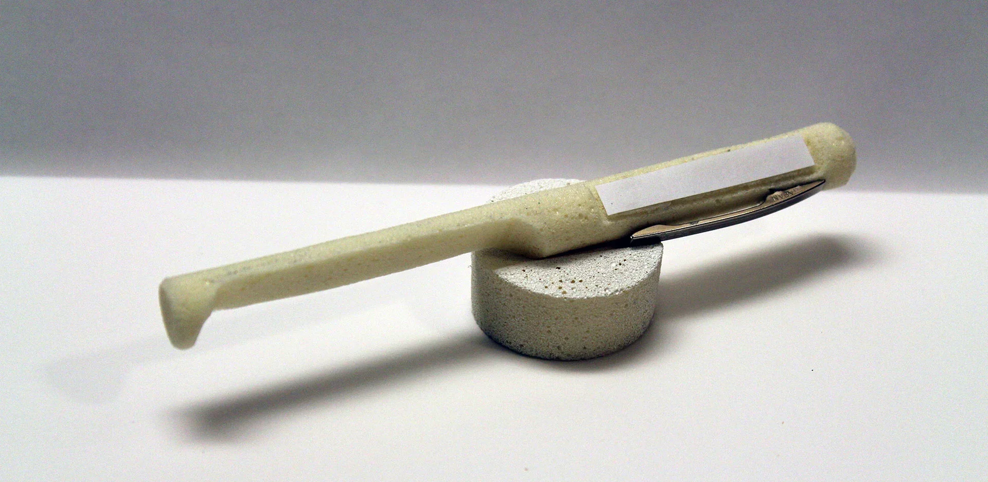 A white cotton swab with a rectangular white label on the handle, resting on a small white cylindrical foam stand against a gray and white background.