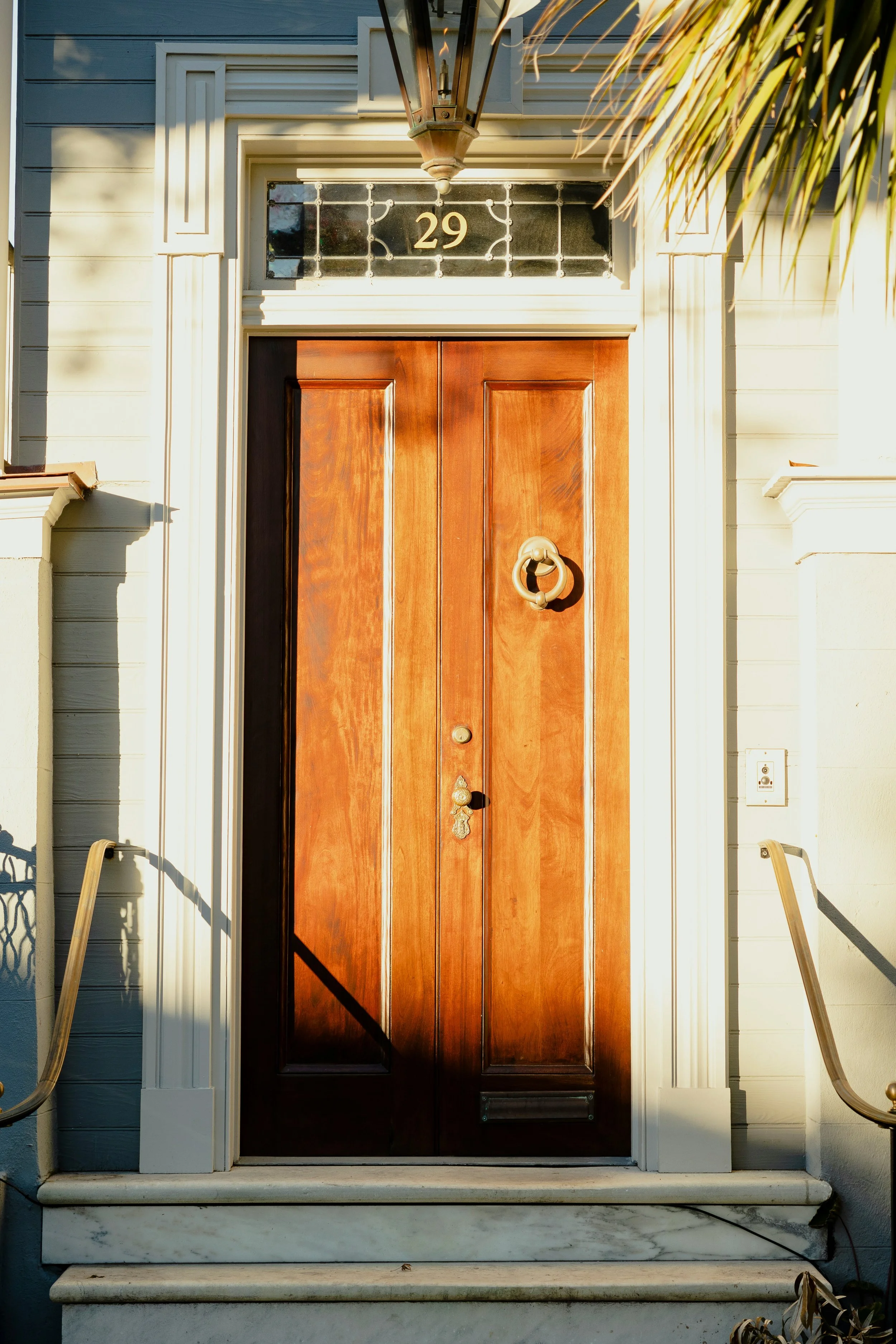 Front door of a house with a wooden door and decorative glass panel above it displaying the number 29, flanked by white trim and columns, with a lantern hanging above.