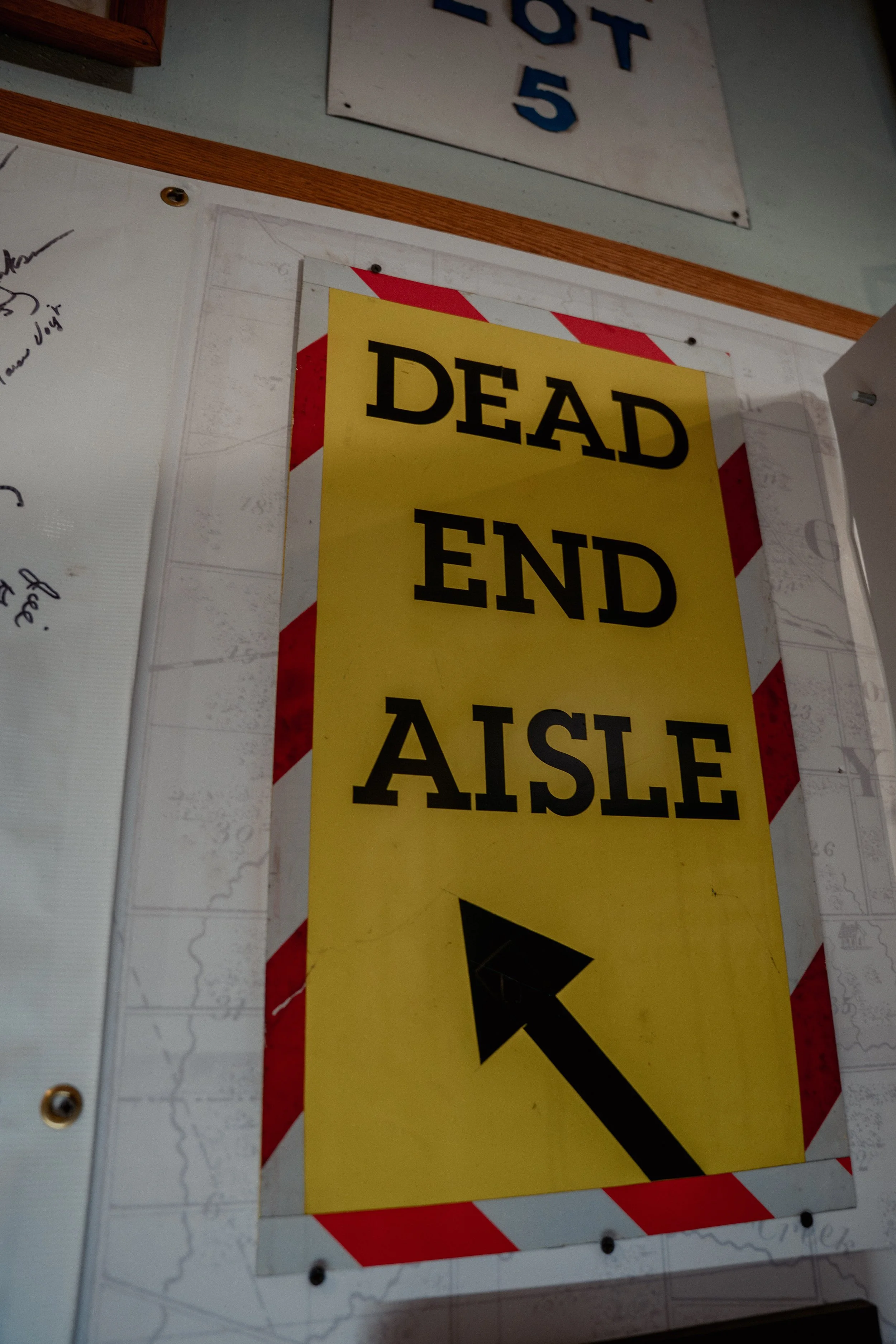 A yellow sign with black text saying 'Dead End' with a red and white striped border, placed on a wall.