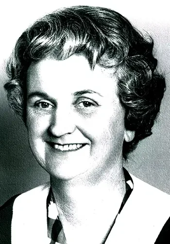 Black and white photograph of a woman with short, curly hair, smiling, wearing a collared shirt and jacket.
