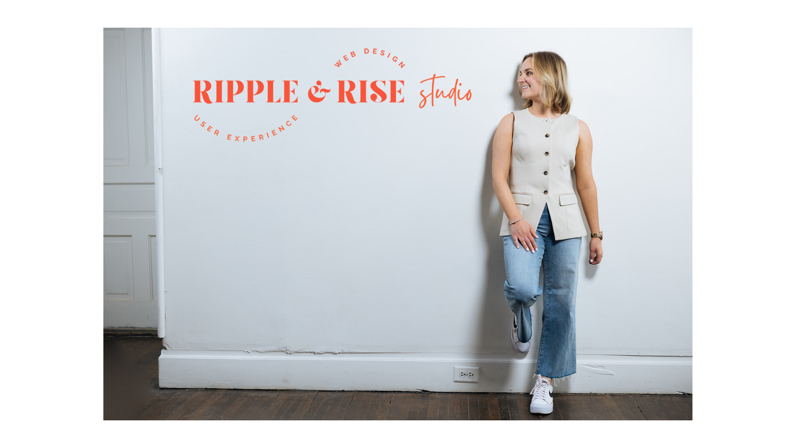 Woman standing against white wall with logo and text for Ripple & Rise Studio, wearing sleeveless cream blazer and jeans, smiling and looking to the side.
