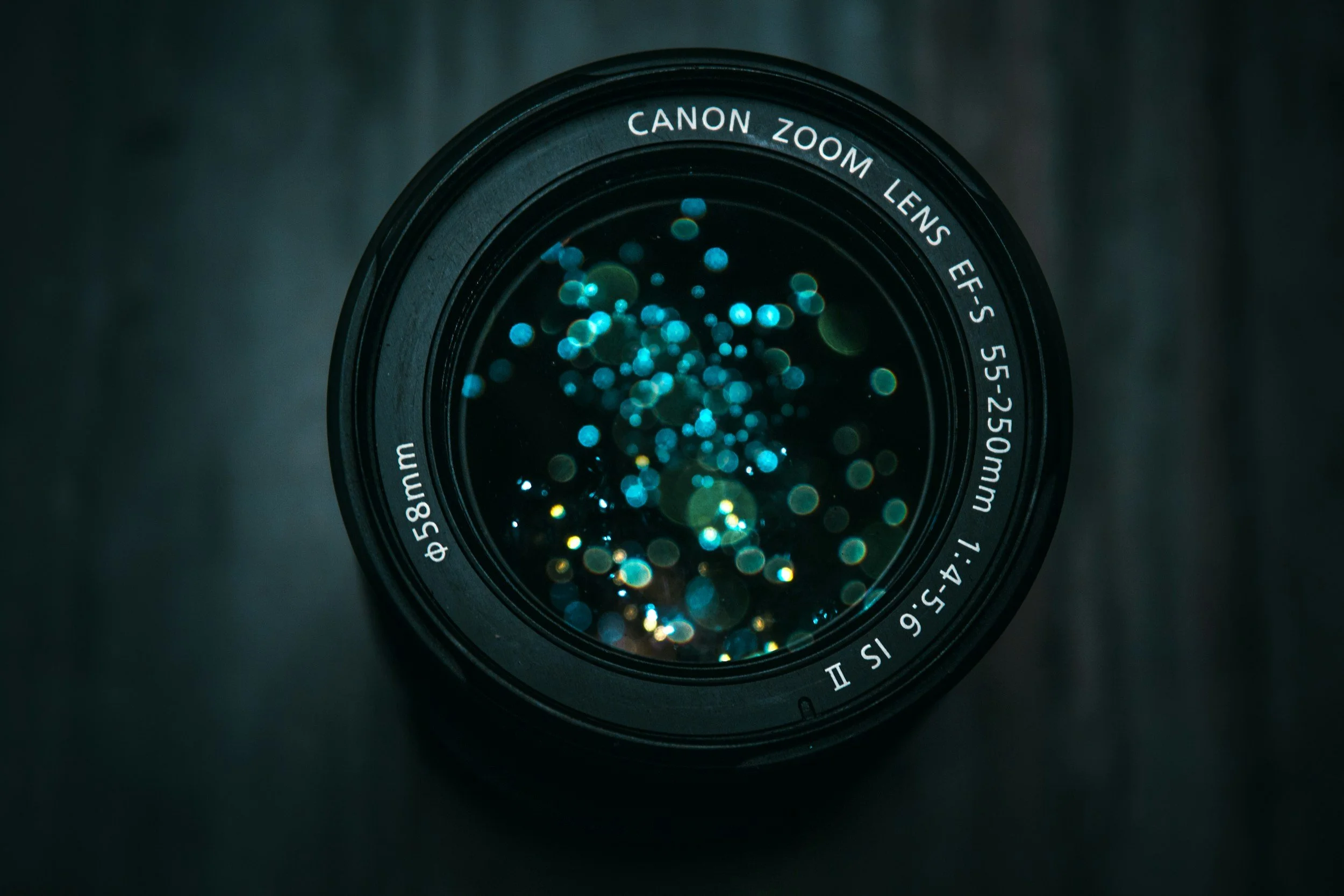 Close-up of a Canon zoom lens with reflections of blue and green bokeh lights in the glass elements.