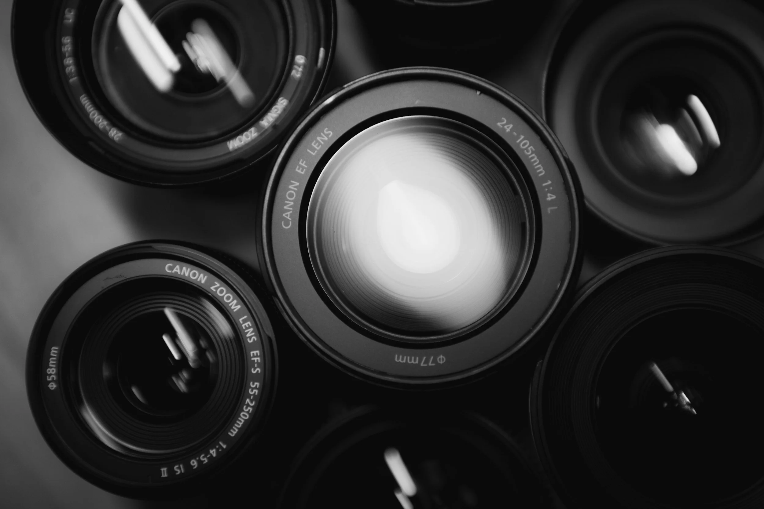 A collection of Canon camera lenses, including a zoom lens with 24-105mm focal length, arranged on a surface for a photo.