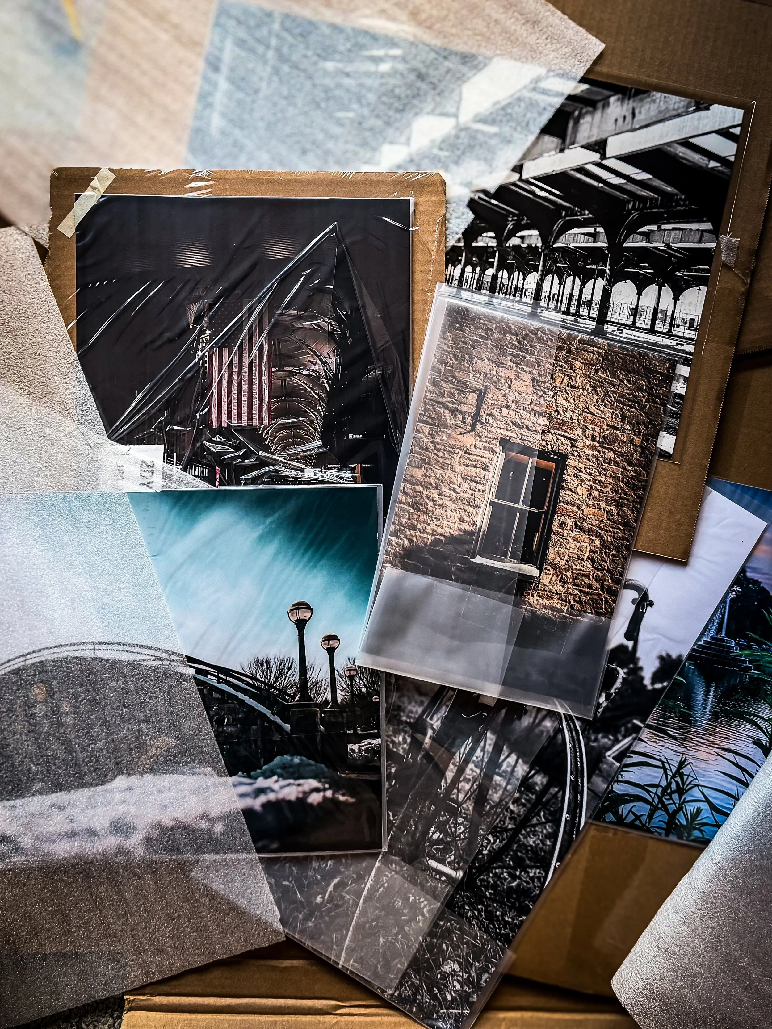 A box of fine art photography prints laid out after delivery while preparing inventory for Spring Fest, featuring bridge photography, architectural details, and black and white artwork.