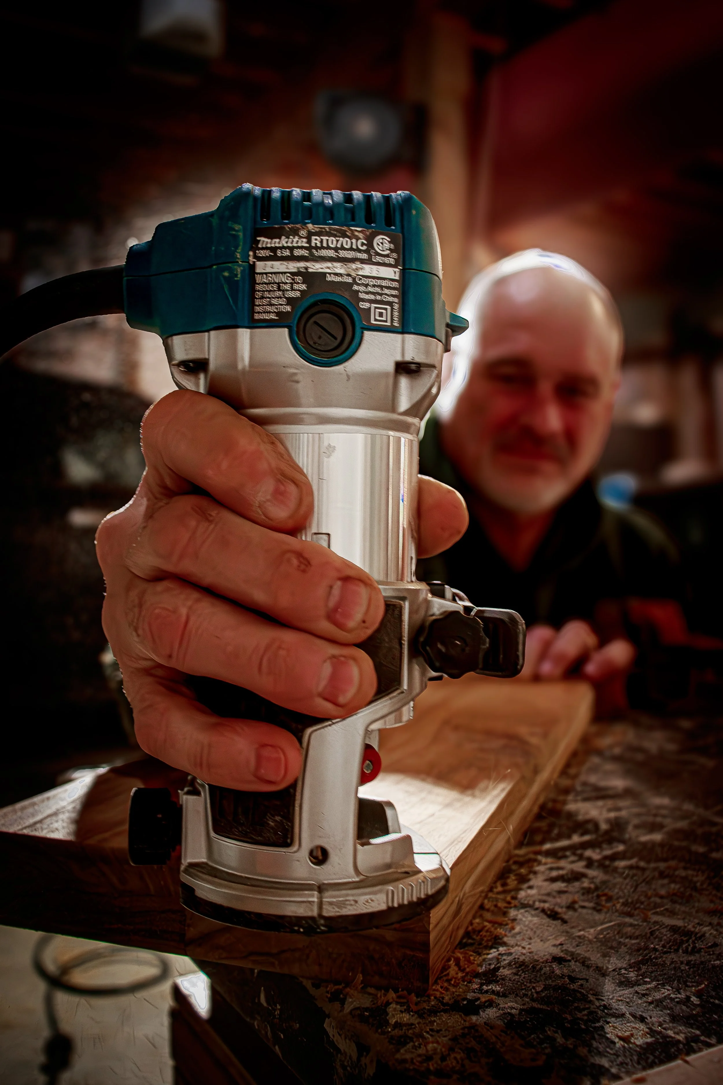 woodworker using a handheld router to carve a wooden cutting board in a workshop, documenting artisan craftsmanship for small business branding