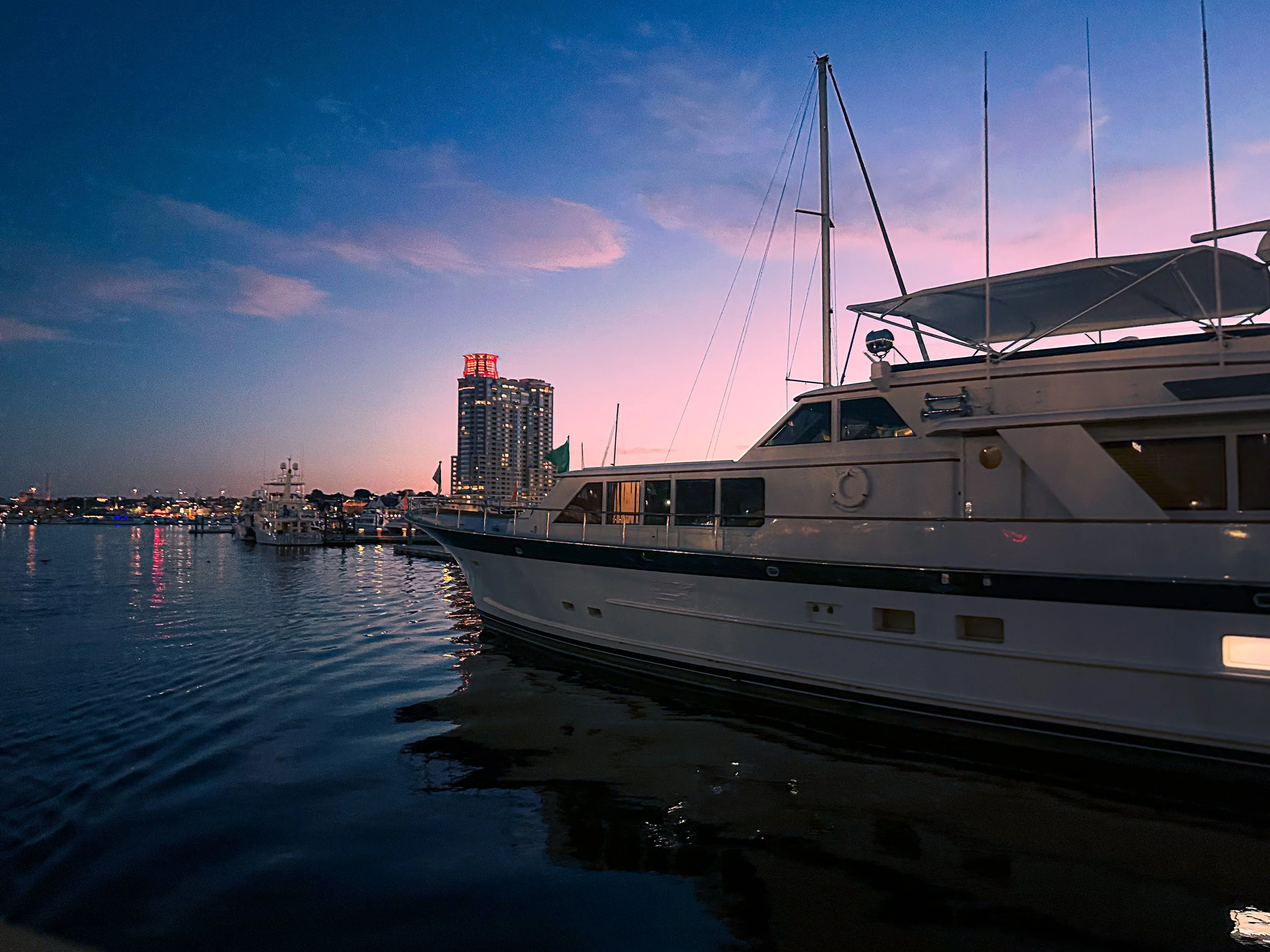 Sailboat resting in calm harbor waters at sunset, reflecting soft evening light along the waterfront skyline.
