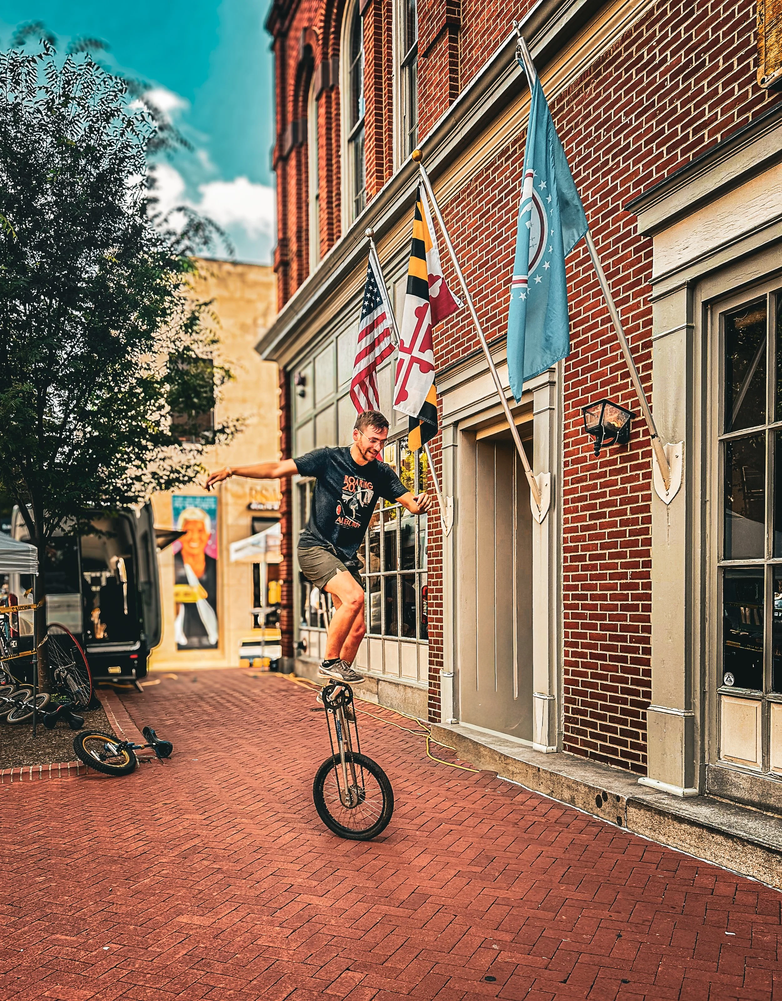Cyclist riding through a historic brick street lined with American flags and classic architecture in a small-town setting.