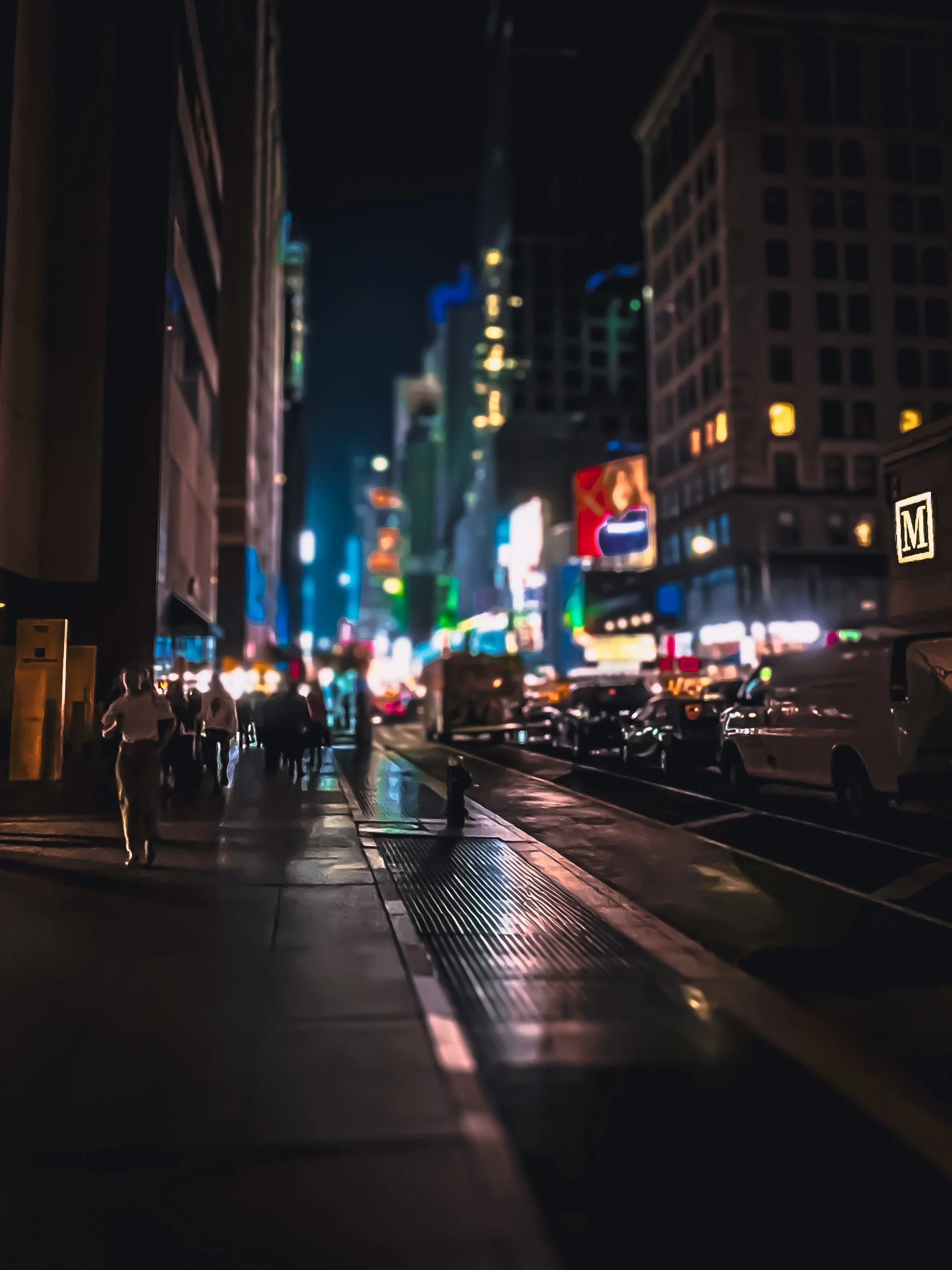 Nighttime city street with illuminated signs, tall buildings, cars parked along the curb, and people walking on the sidewalk.