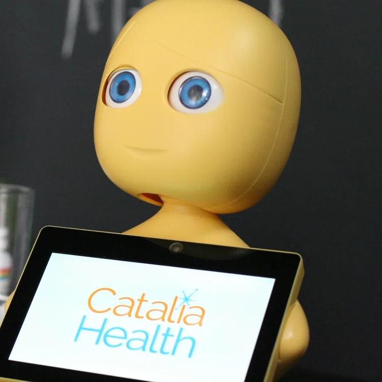 Mabu, a robot with a large yellow head and blue eyes holding a tablet displaying the words 'Catalia Health'.