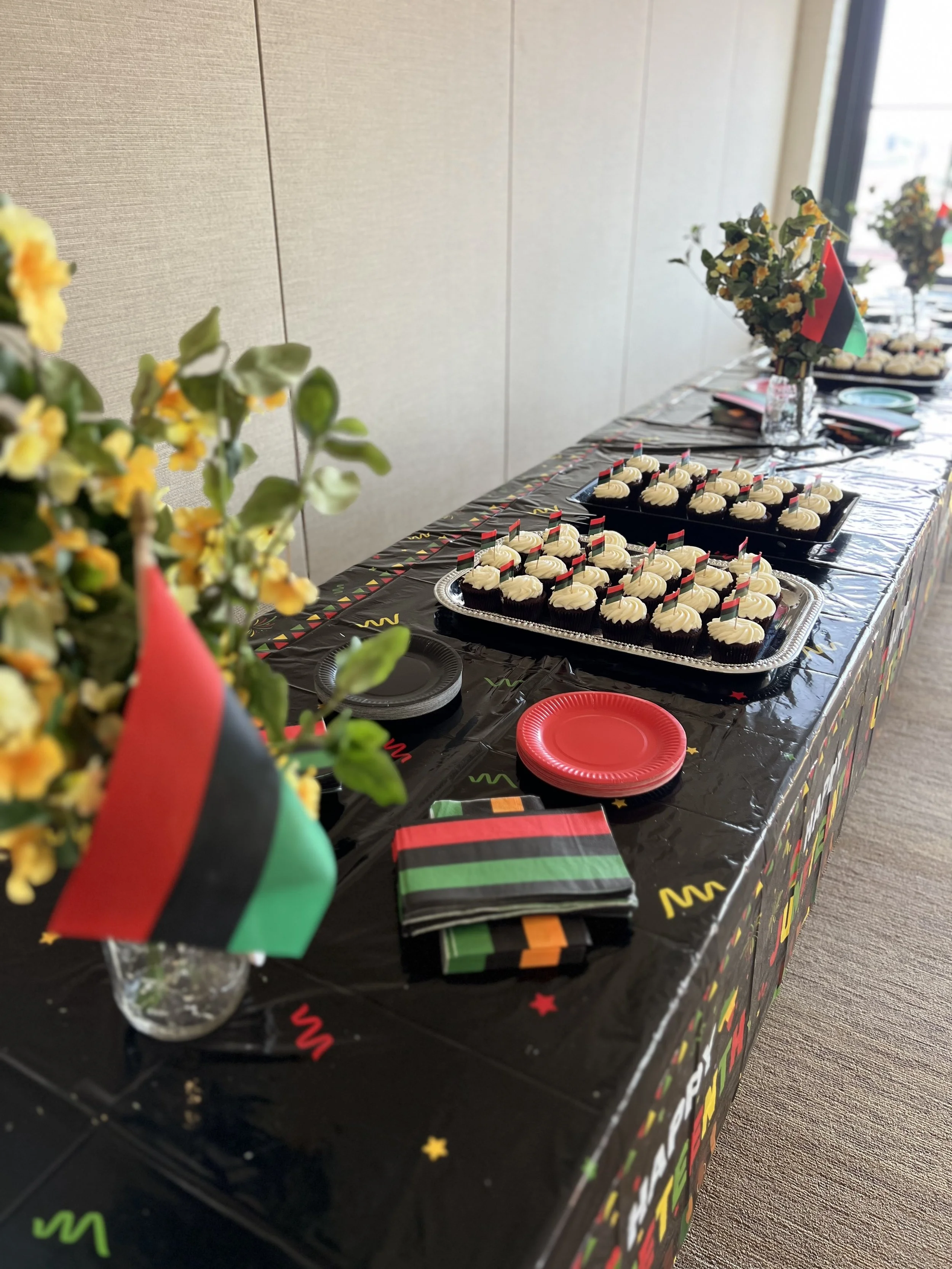 Party table with cupcakes, napkins, and plates, decorated with red, green, black, and orange colors, featuring flags and flowers, celebrating with a theme related to Malawi.
