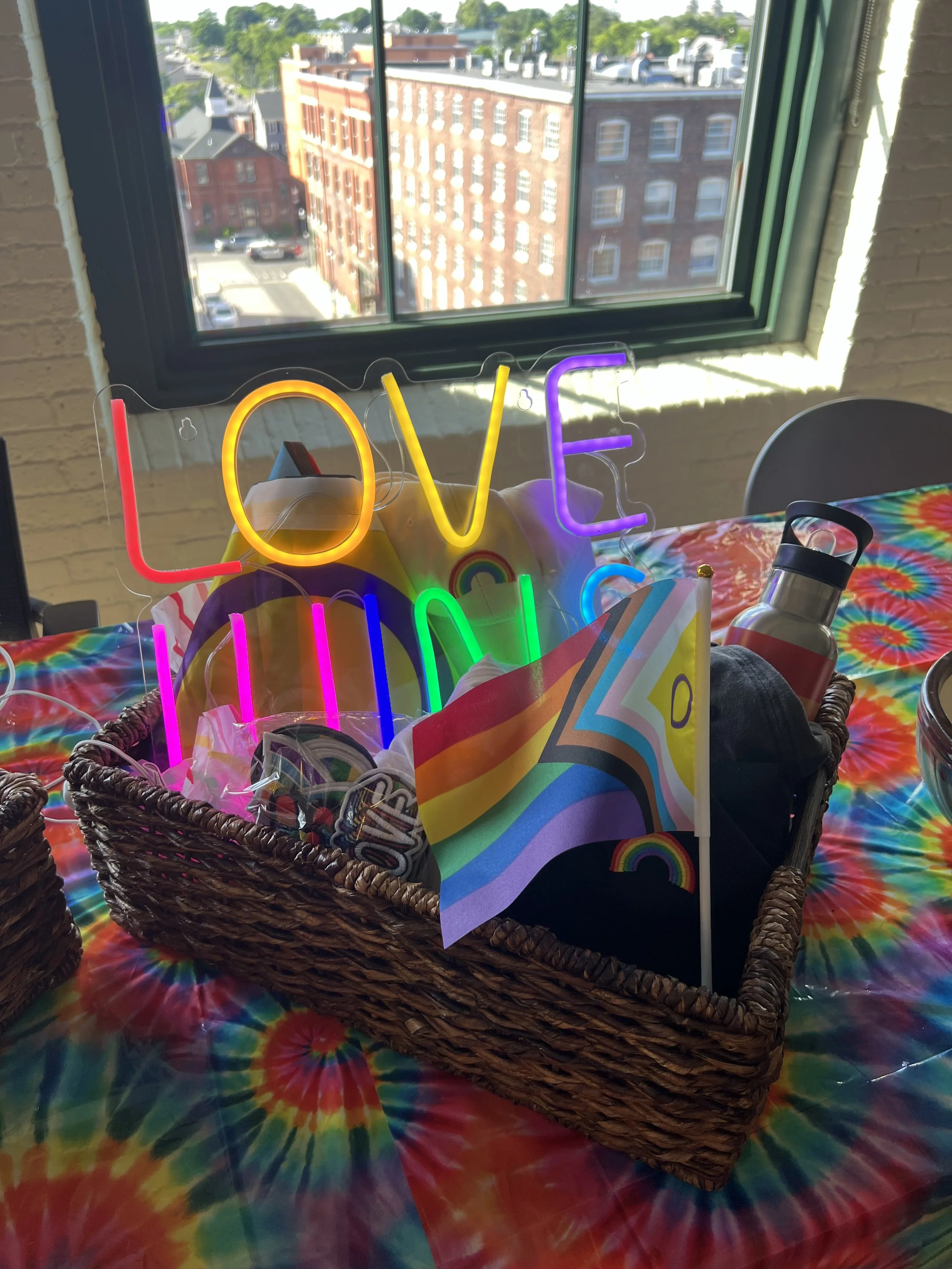 Table decorated with a tie-dye tablecloth, featuring a wicker basket holding a rainbow flag, a neon 