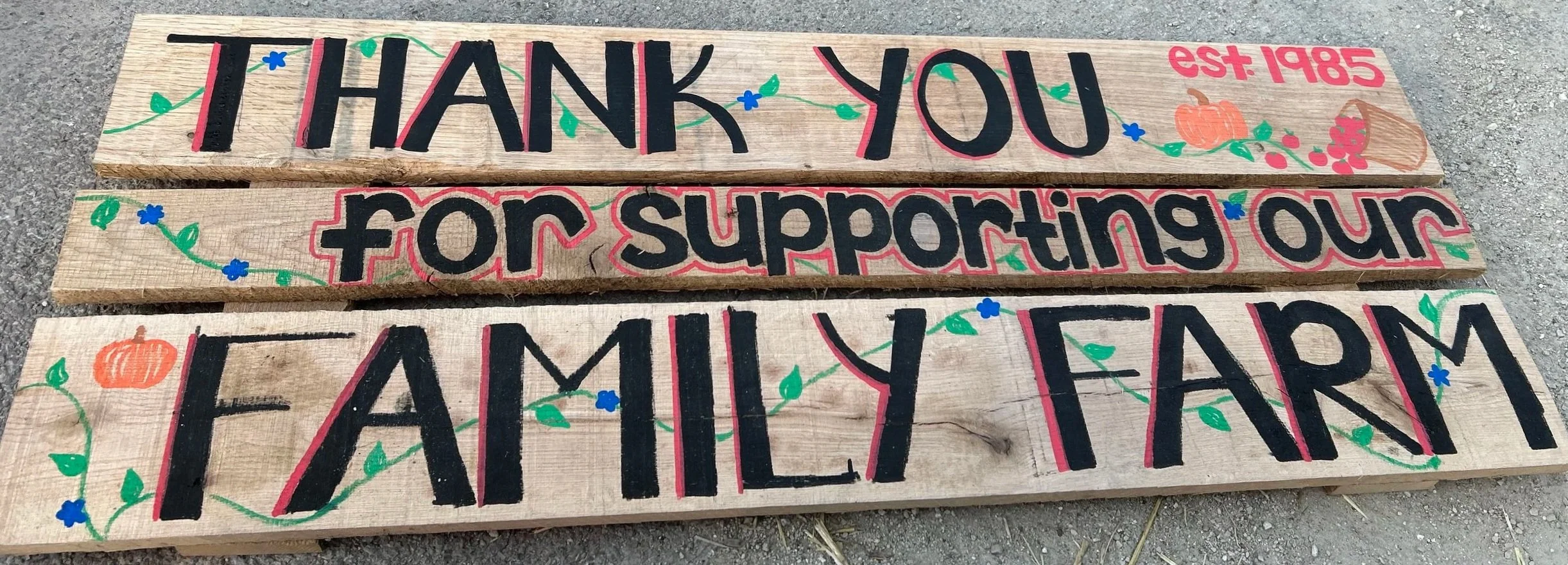 Wooden signboard with hand-painted message that reads "Thank You for Supporting Our Family Farm" in colorful letters with decorative pumpkins, berries, and vines.